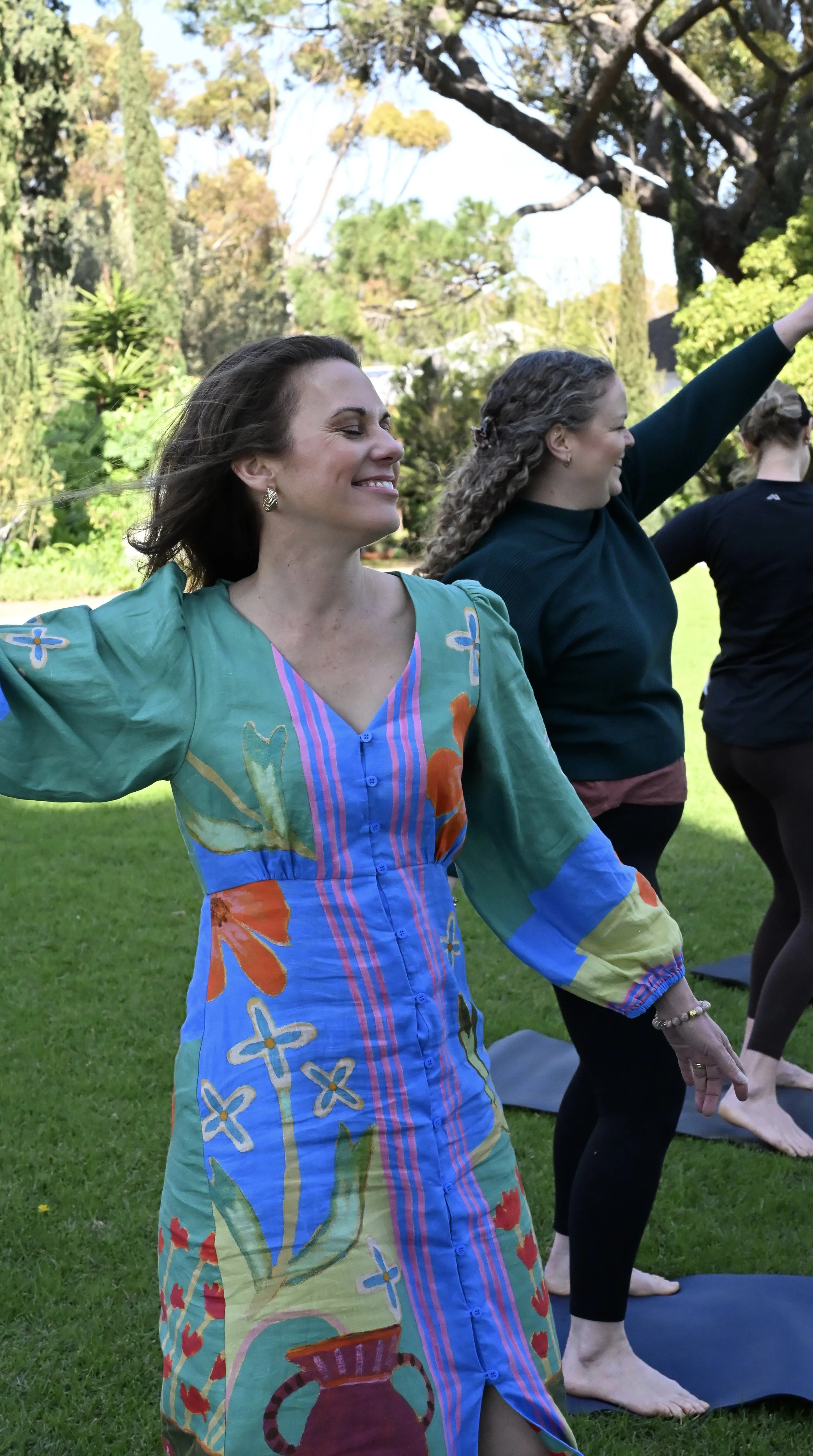 Women participating in outdoor yoga or stretching session on grassy lawn with trees in background.