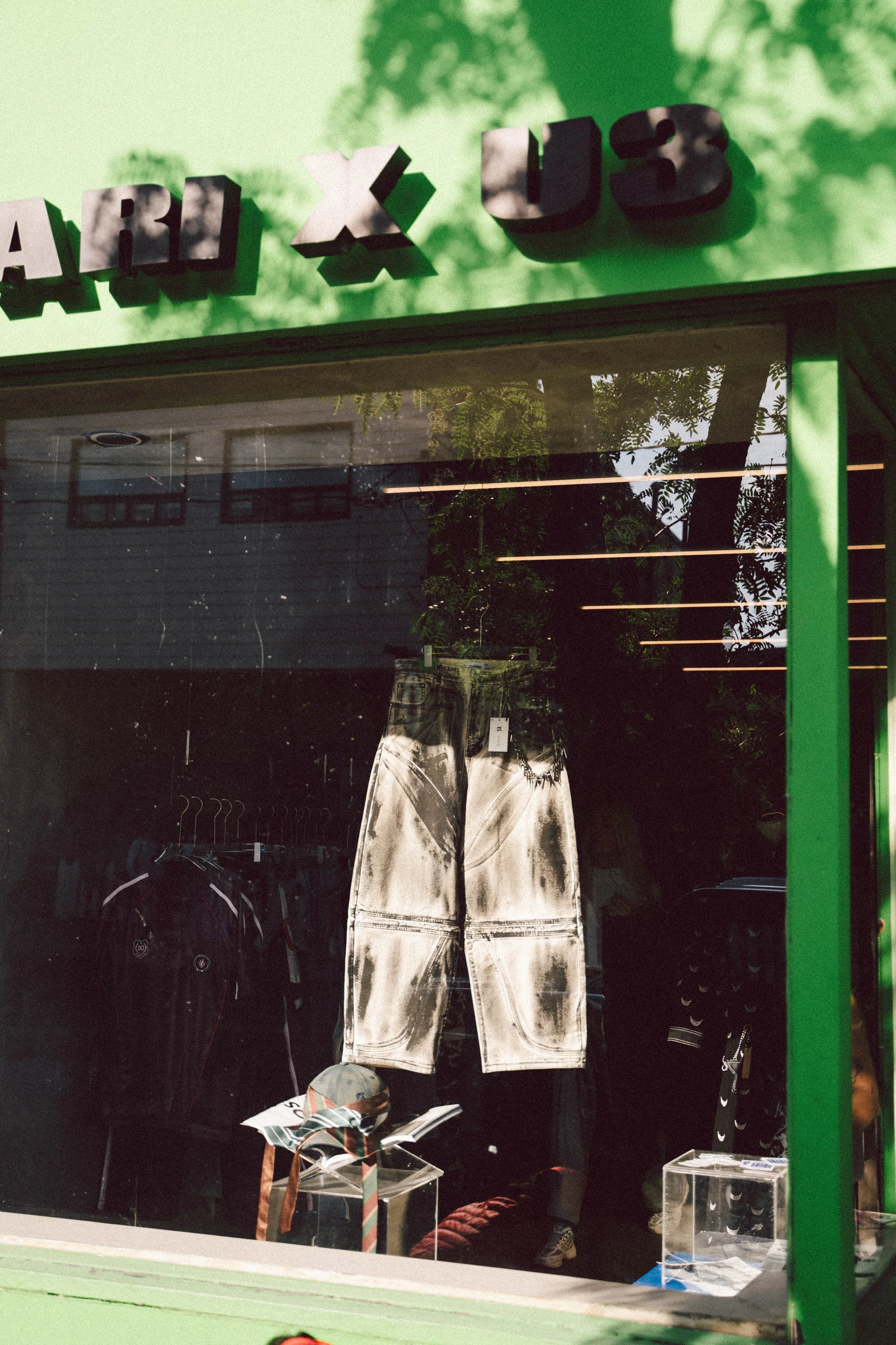 Clothing store window display with white pants, black jacket, and various accessories, behind glass.