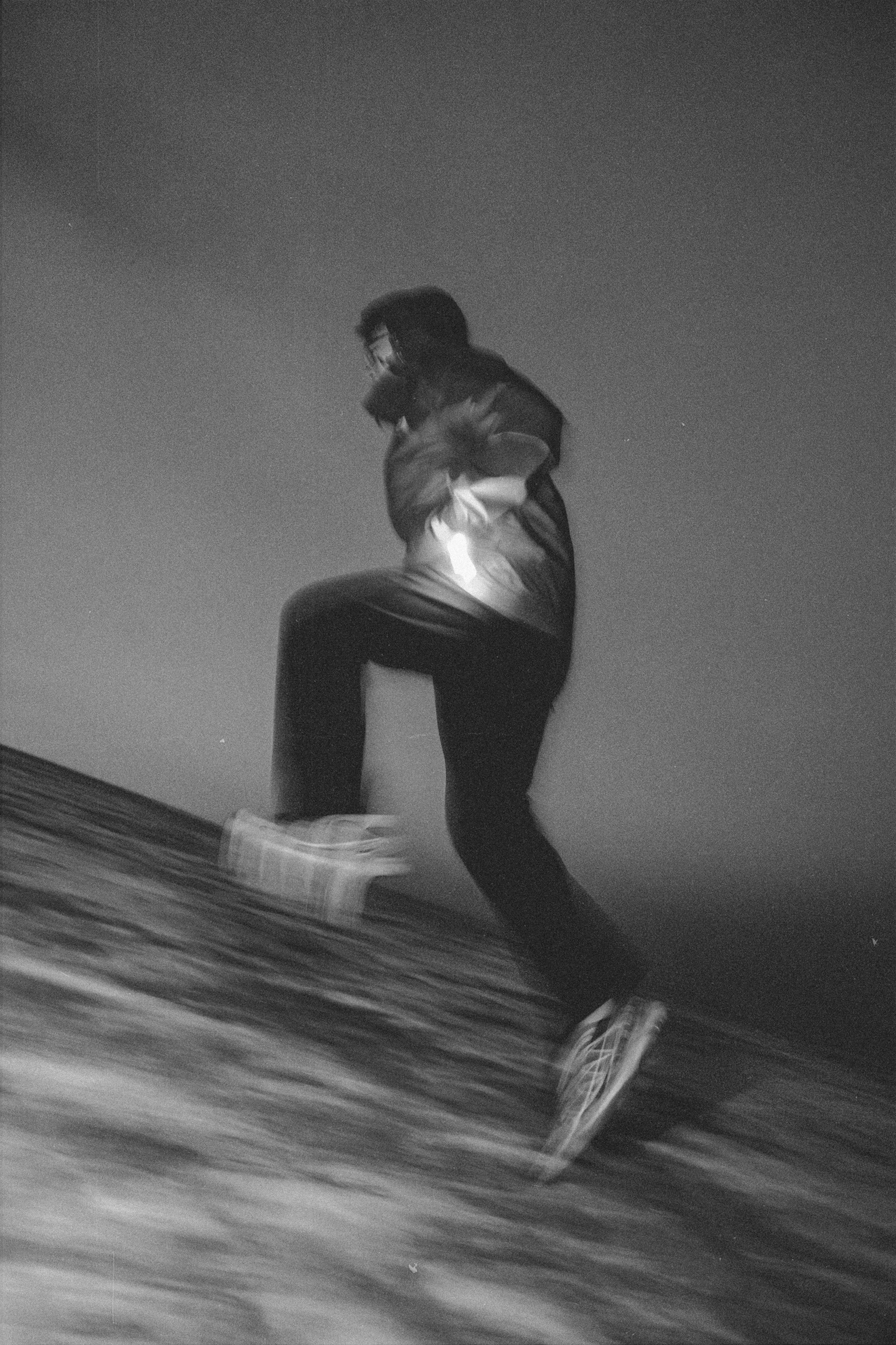 A black and white photo of a person running up a hill outdoors at night, with a clear sky in the background.