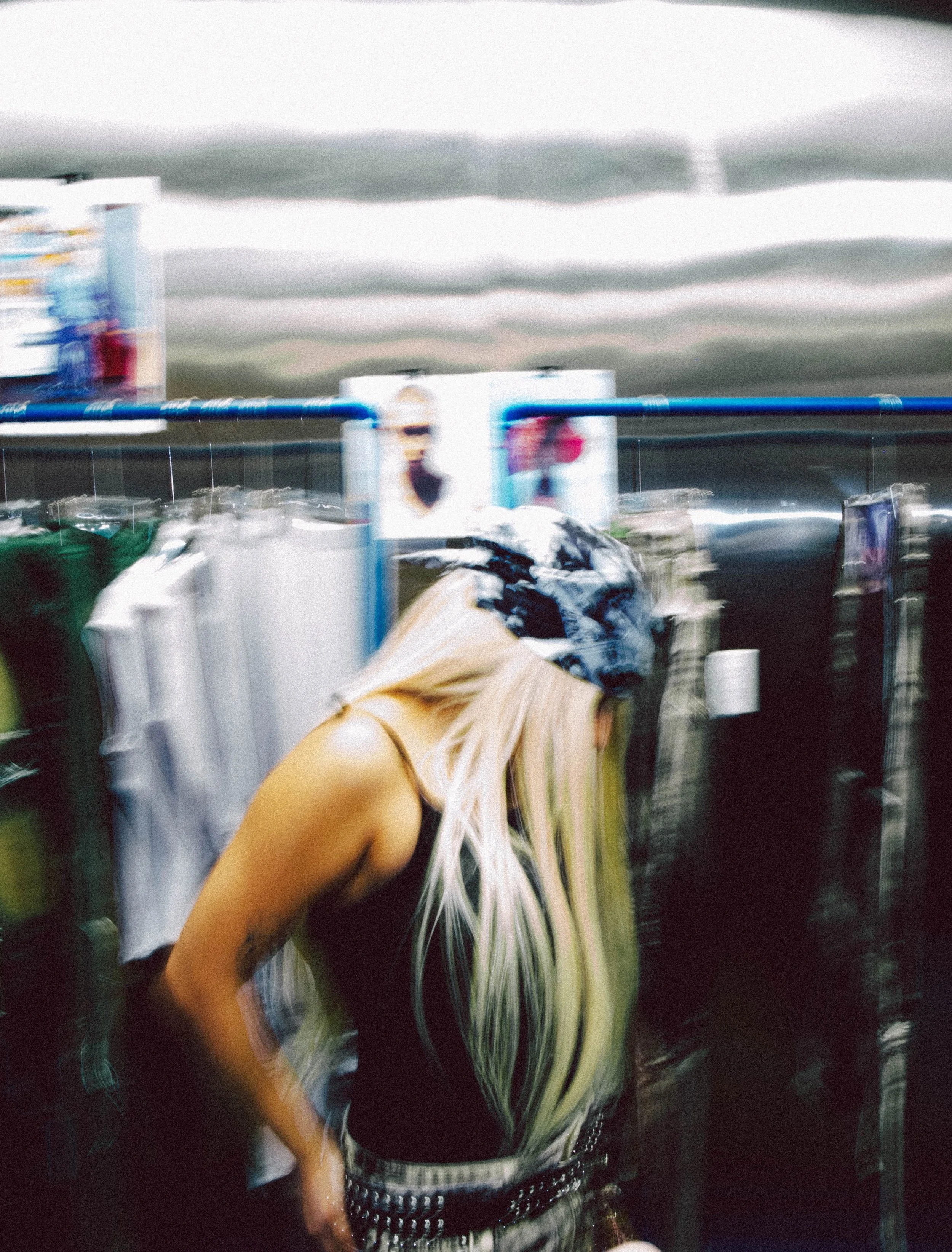A woman with long, platinum blonde hair wearing a bandana shopping in a clothing store.