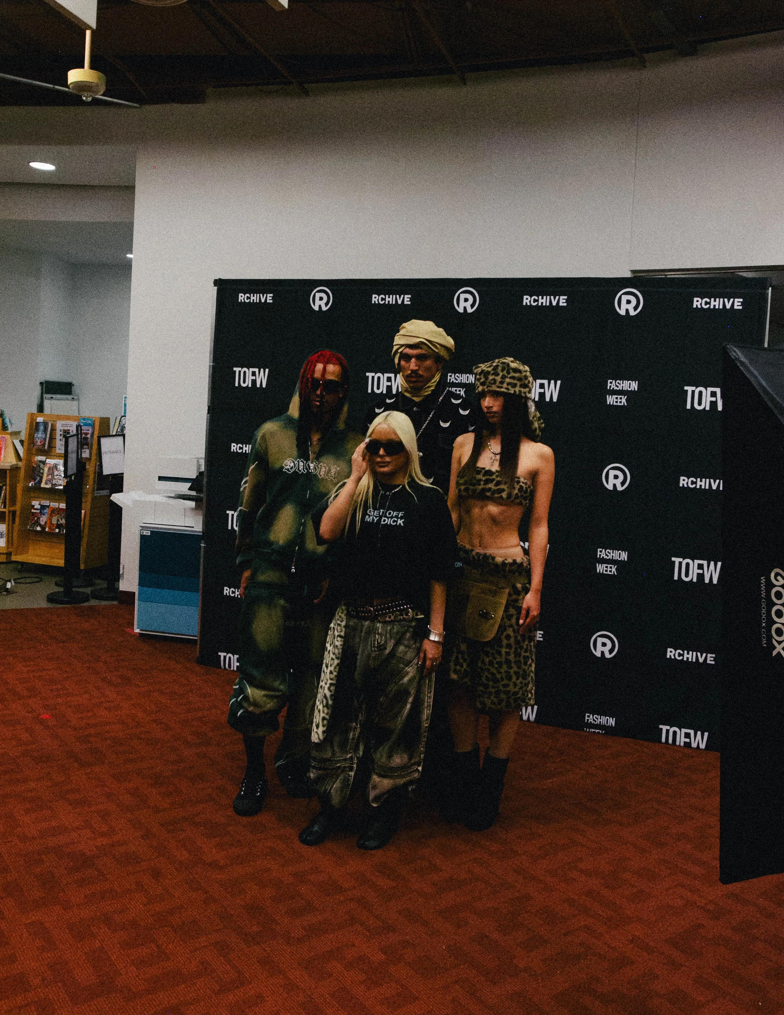 Group of four diverse models posing in front of a black backdrop with fashion-related logos at a fashion week event.