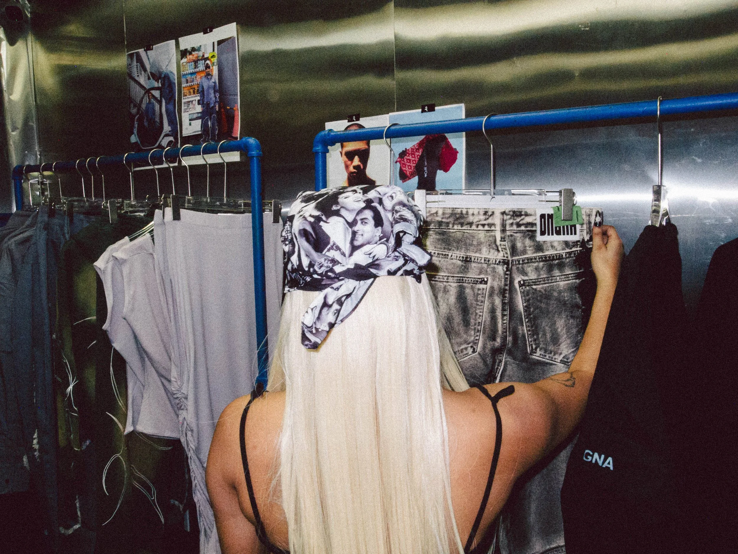 A woman with long blonde hair trying on Levi's shorts in a clothing store, with racks of clothes and posters in the background.