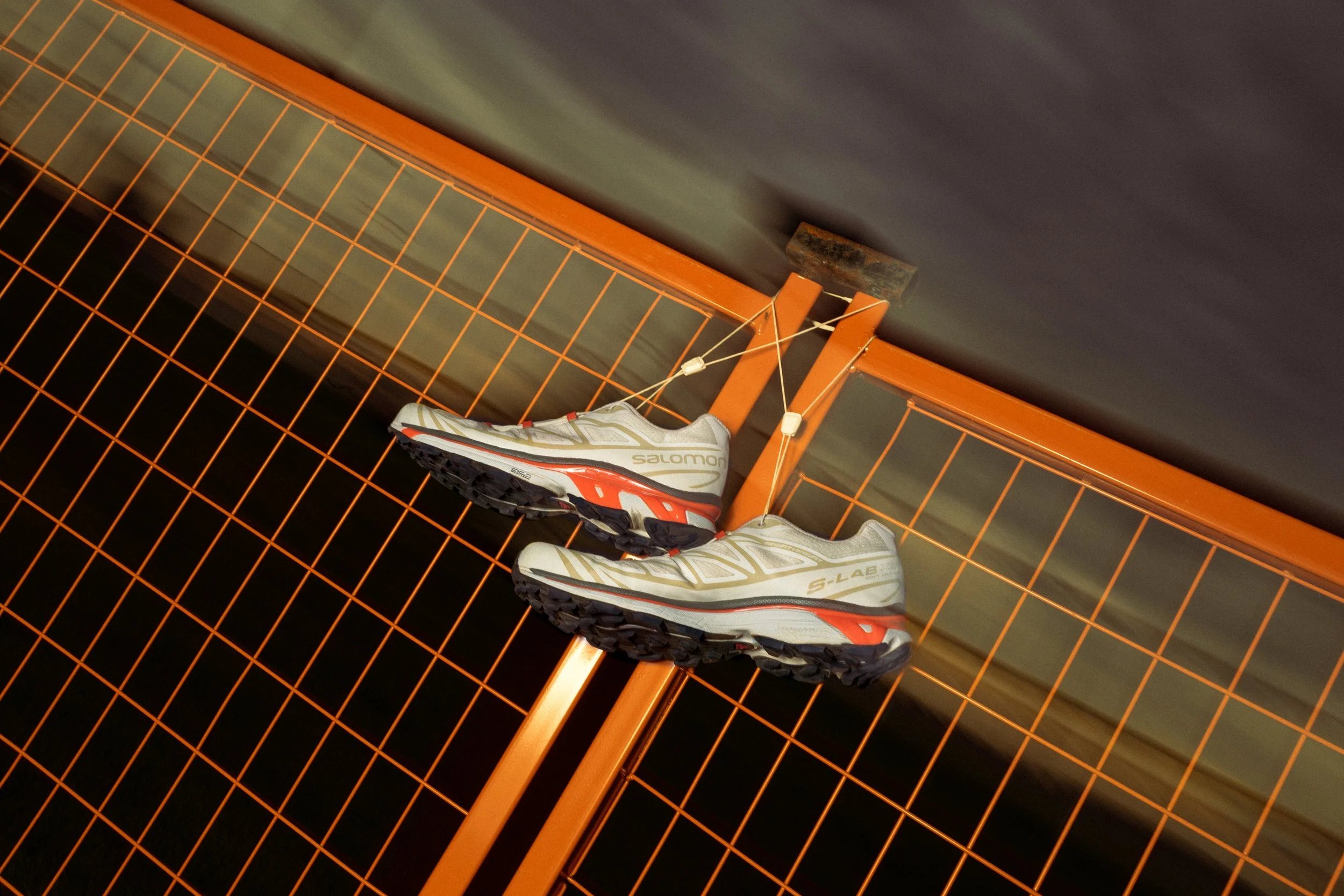 A pair of Salomon trail running shoes hanging on a wire grid with orange framing.