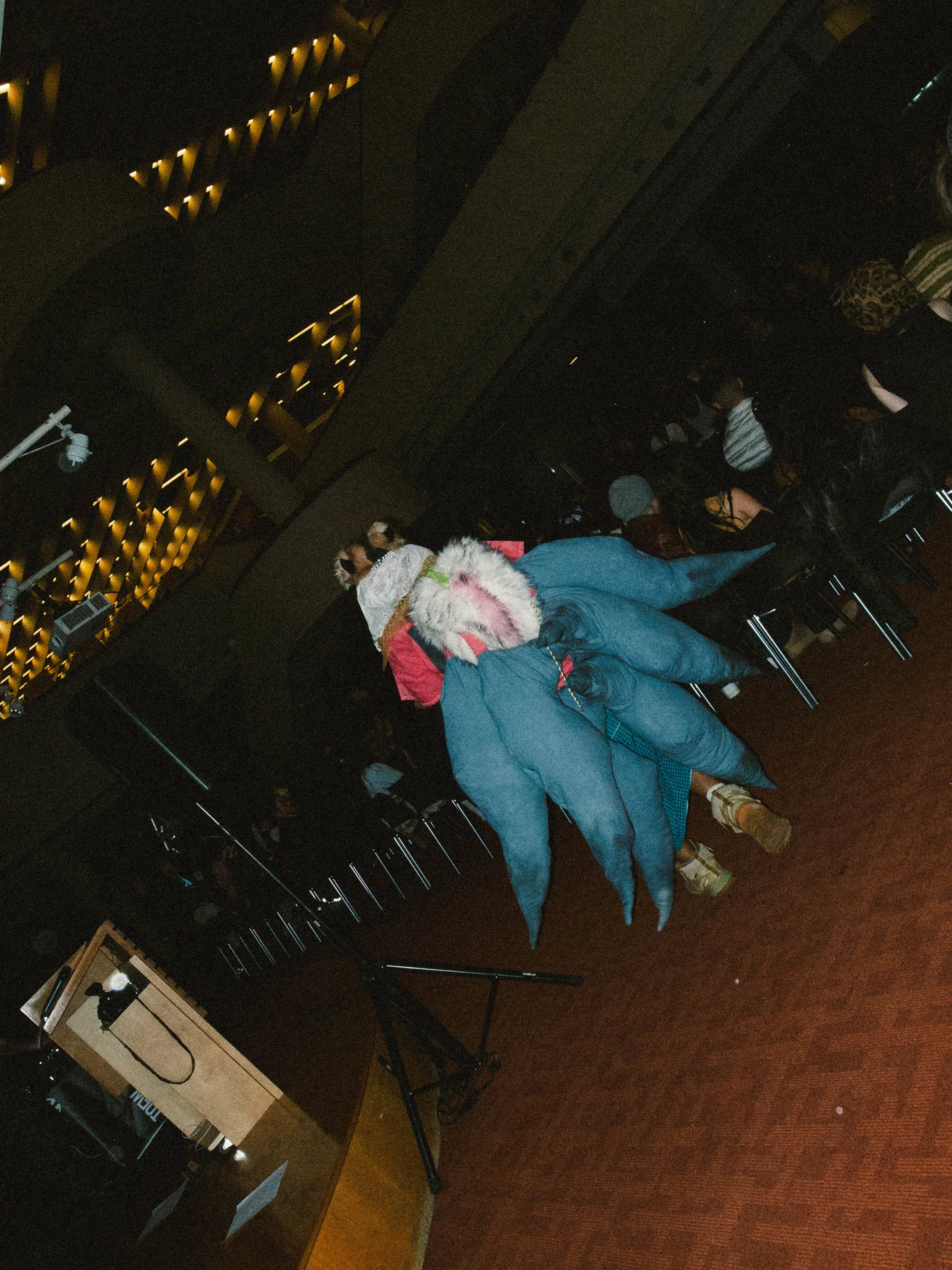 Person sitting in a dark room, possibly at an event or presentation, with several people seated around.