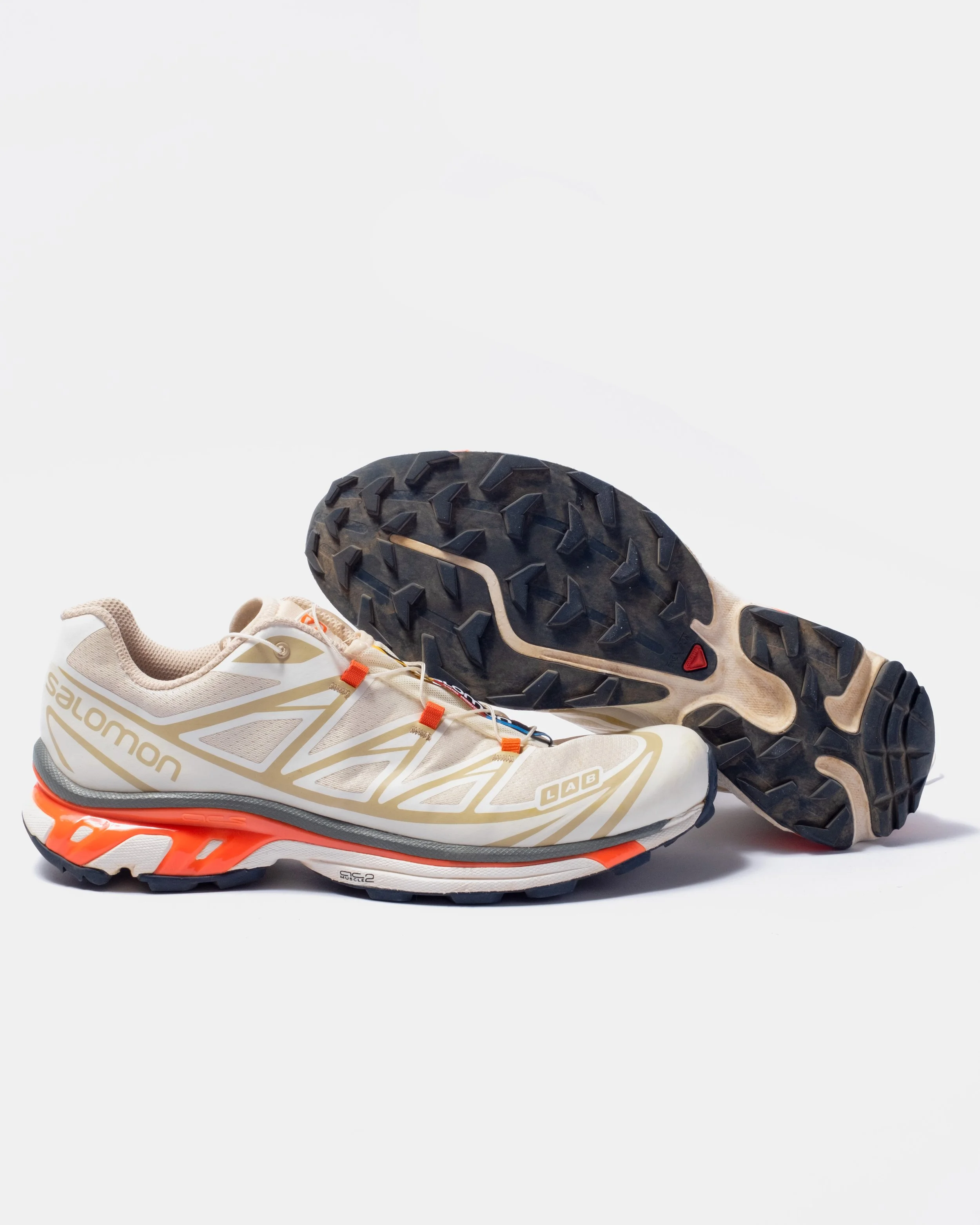 A pair of Salomon trail running shoes with a beige and orange design, positioned against a plain white background.