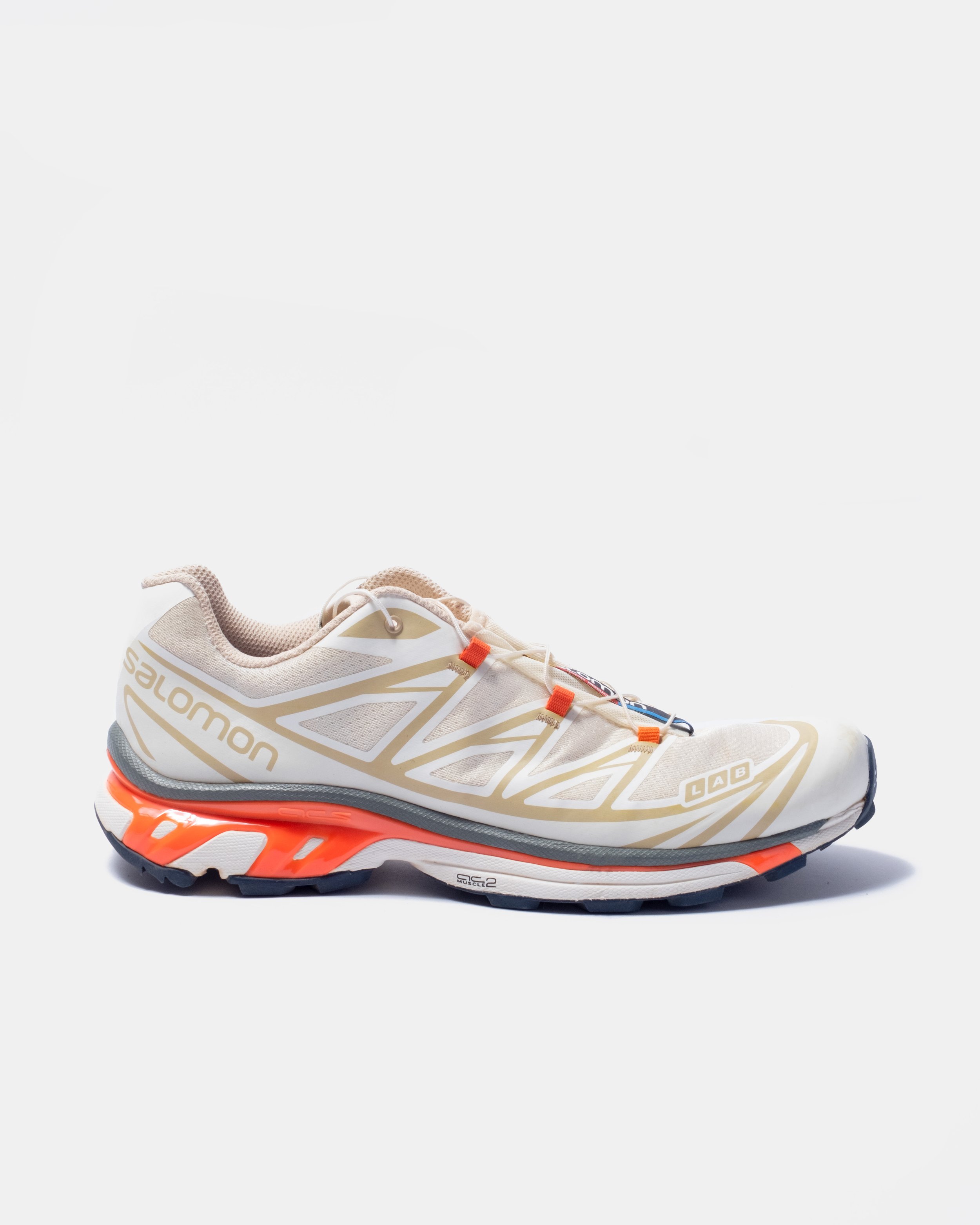 A white and beige Salomon xt6  running shoe with orange accents on a plain background.