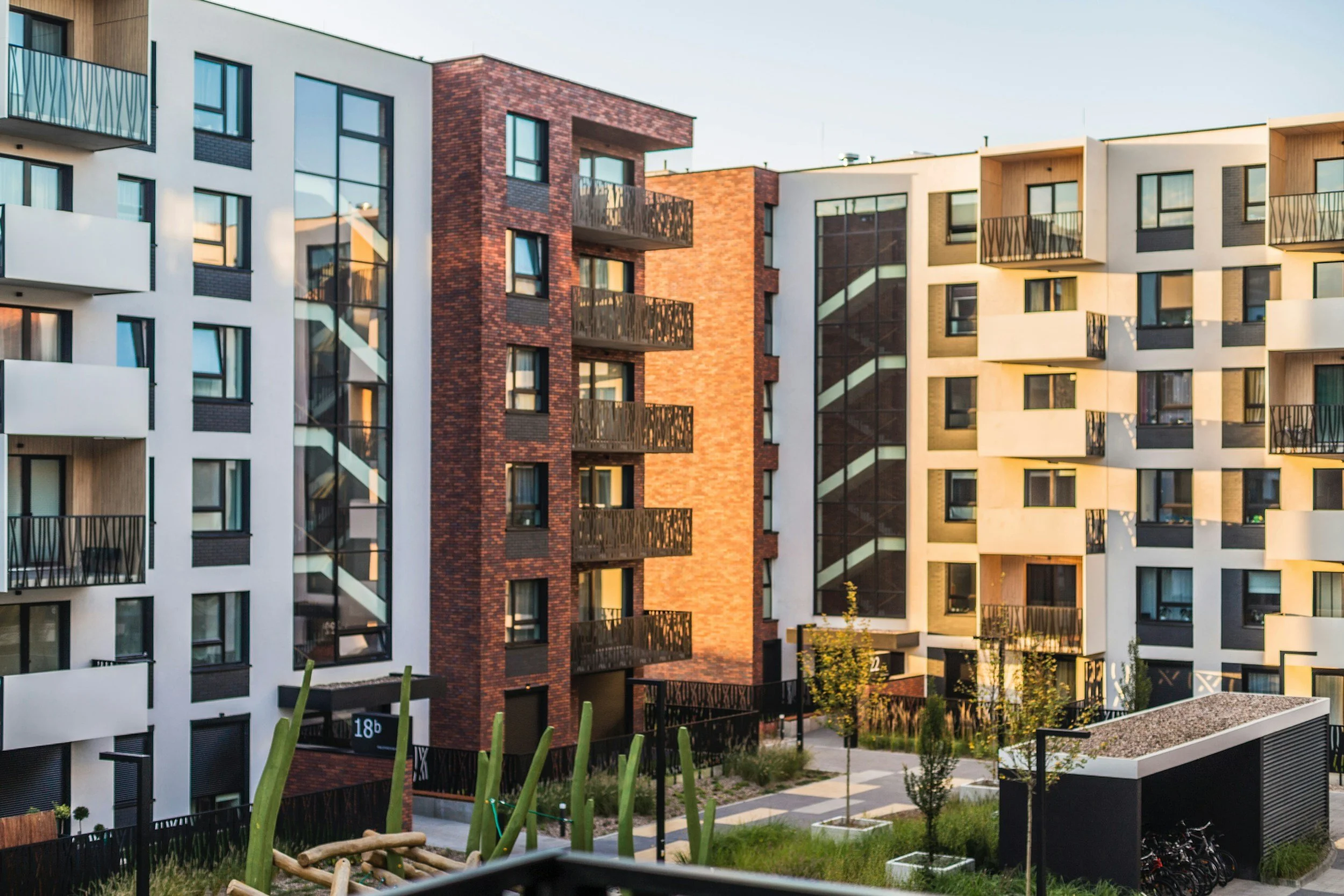 Modern multi-story apartment buildings with balconies and large windows, surrounded by landscaped greenery and a small courtyard.