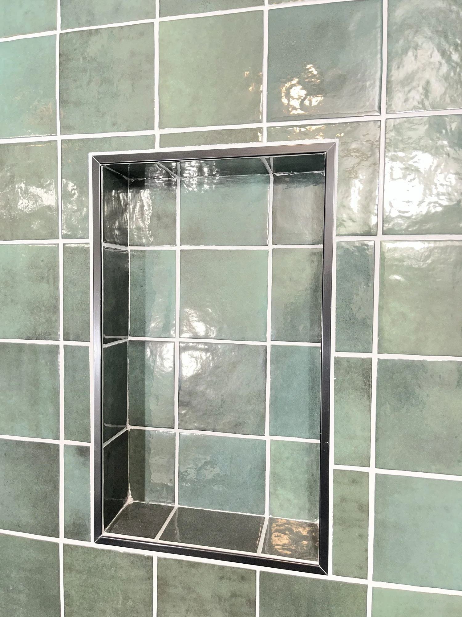 Recessed shower niche framed in green handmade-look tile