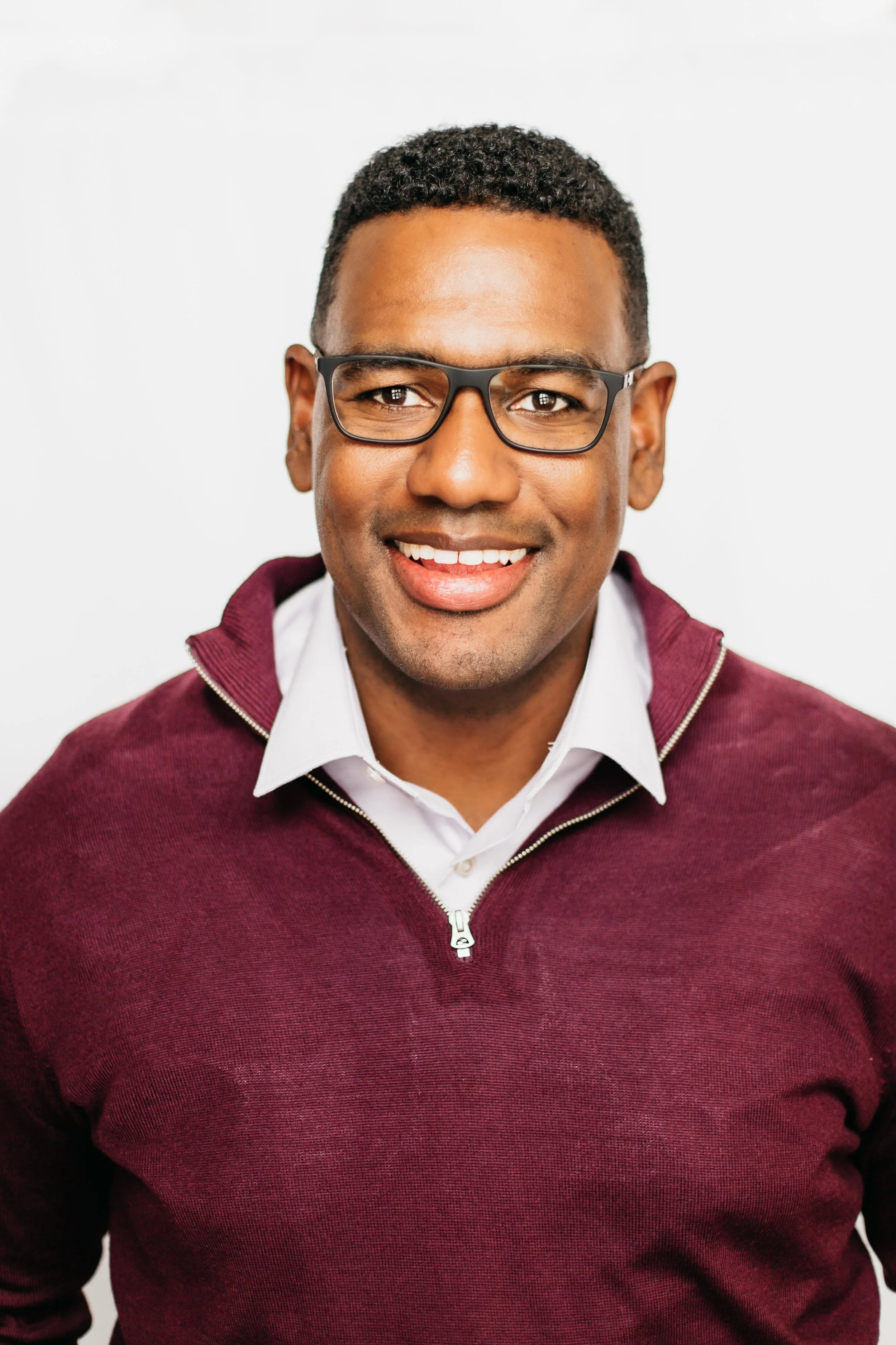 Jaiah Kamara, founder of Signal to Summit Consulting, wearing glasses and a maroon sweater against a white background.