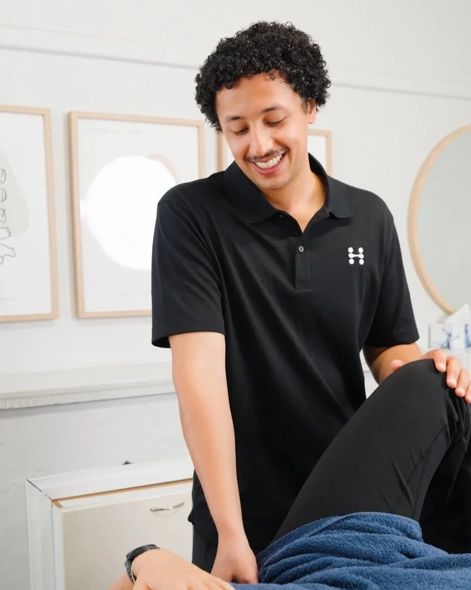 A woman receiving physical therapy treatment, using her hand to hold the patient's hand while smiling.