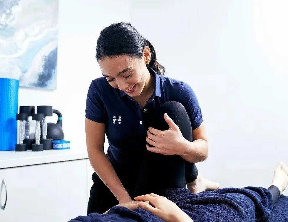 A woman receiving physical therapy treatment, using her hand to hold the patient's hand while smiling.