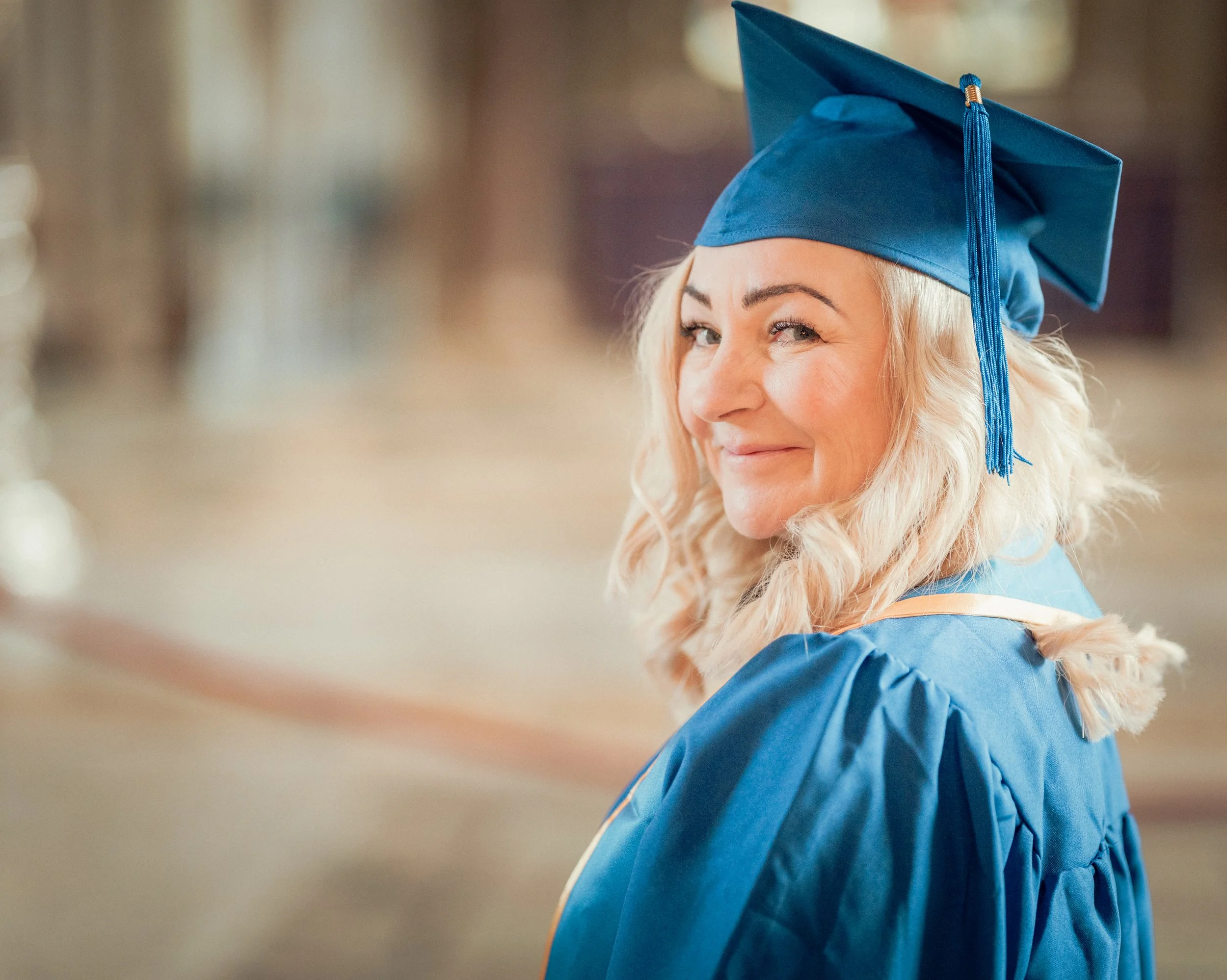 Woman in a blue graduation gown and cap, winking and smiling at the camera.