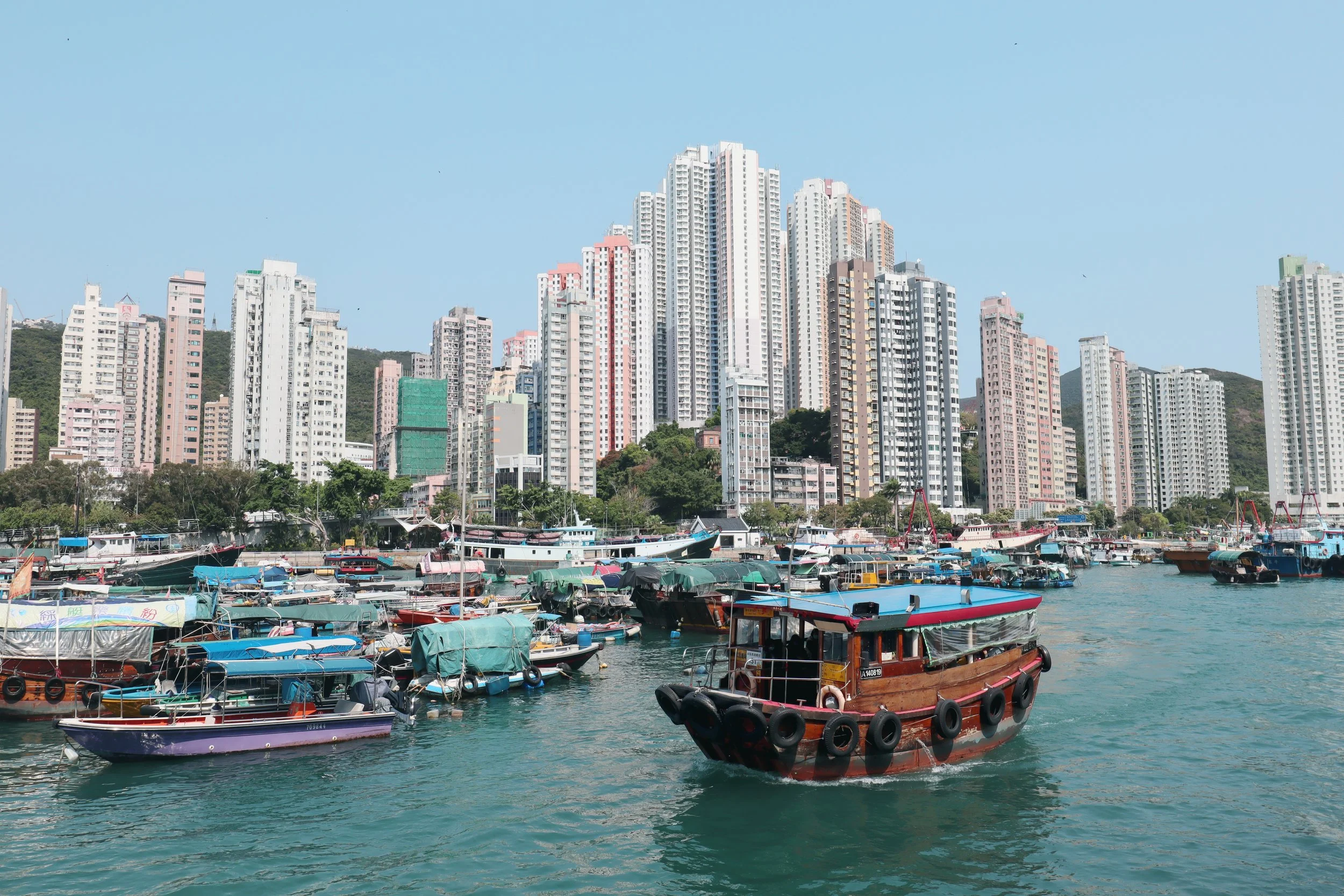 Boats docked in a harbor with high-rise buildings in the background under a clear blue sky.