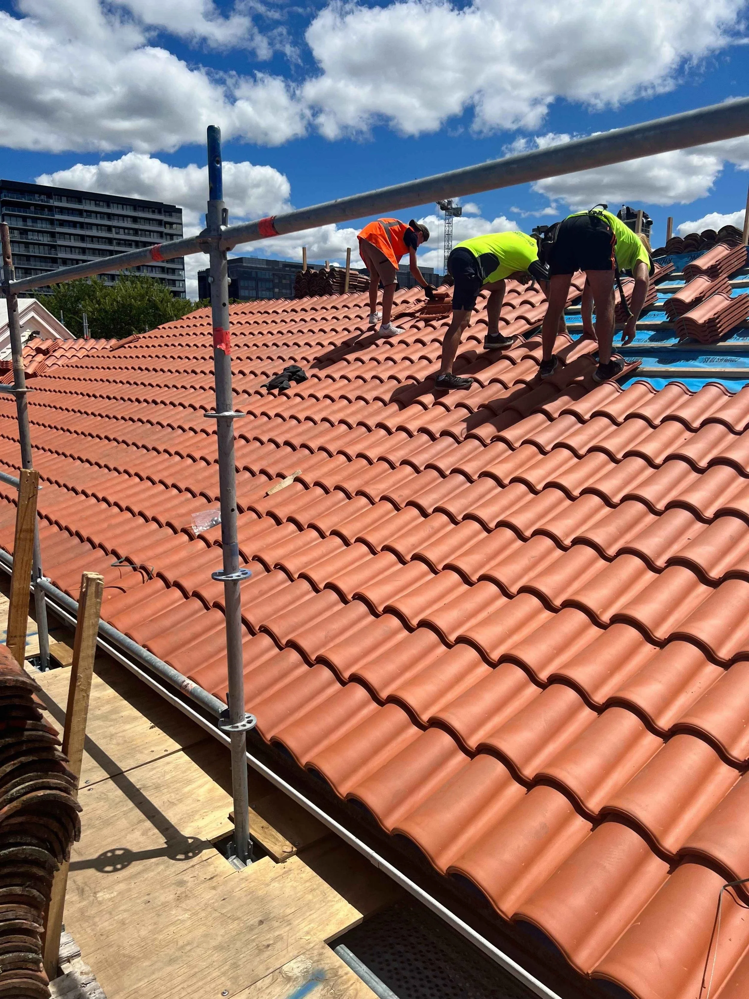 Three roofers installing roof tiles on a pitched roof.