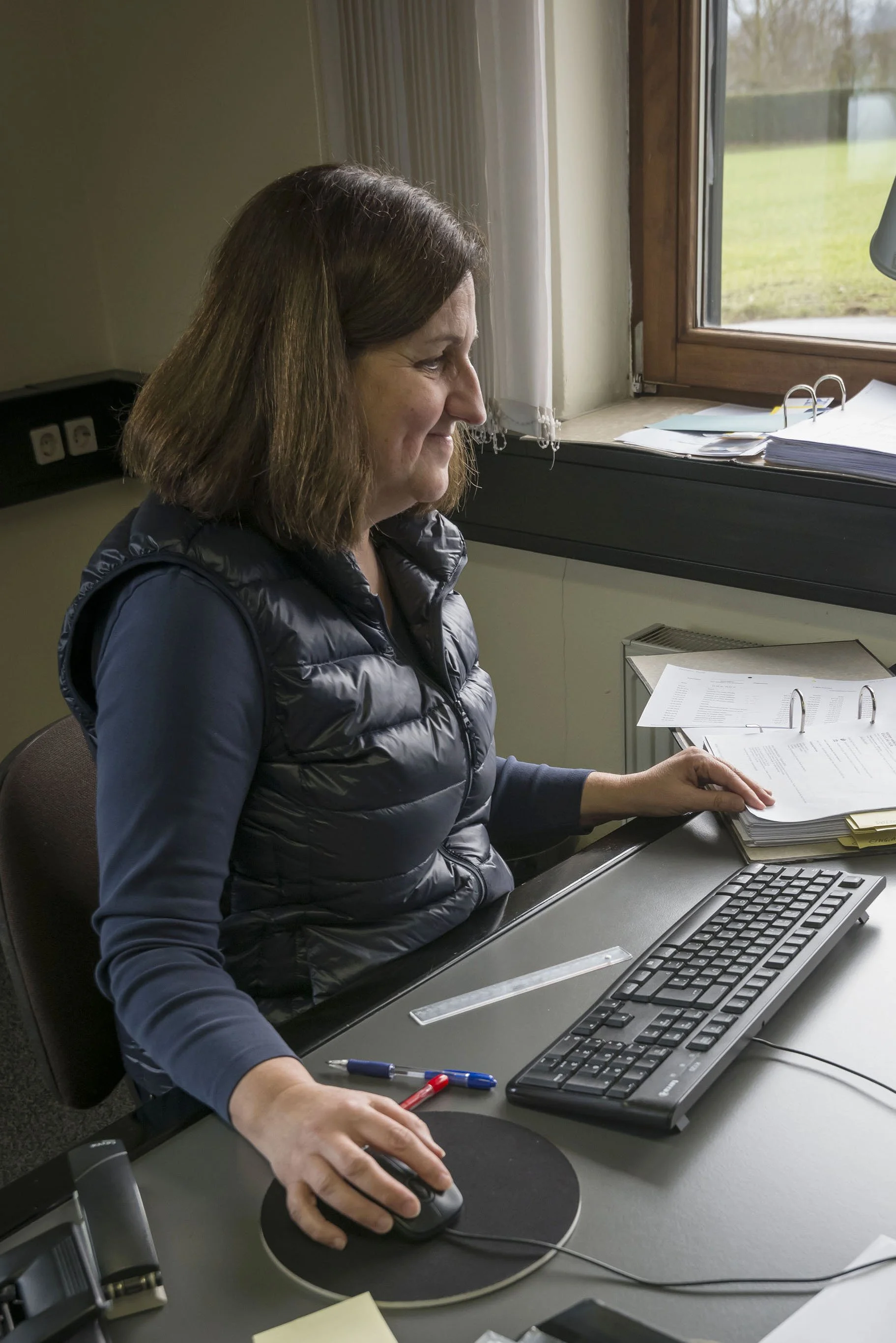 Frau arbeitet im Büro am Schreibtisch, beim Arbeiten am Computer, mit Papieren und Schreibwaren.