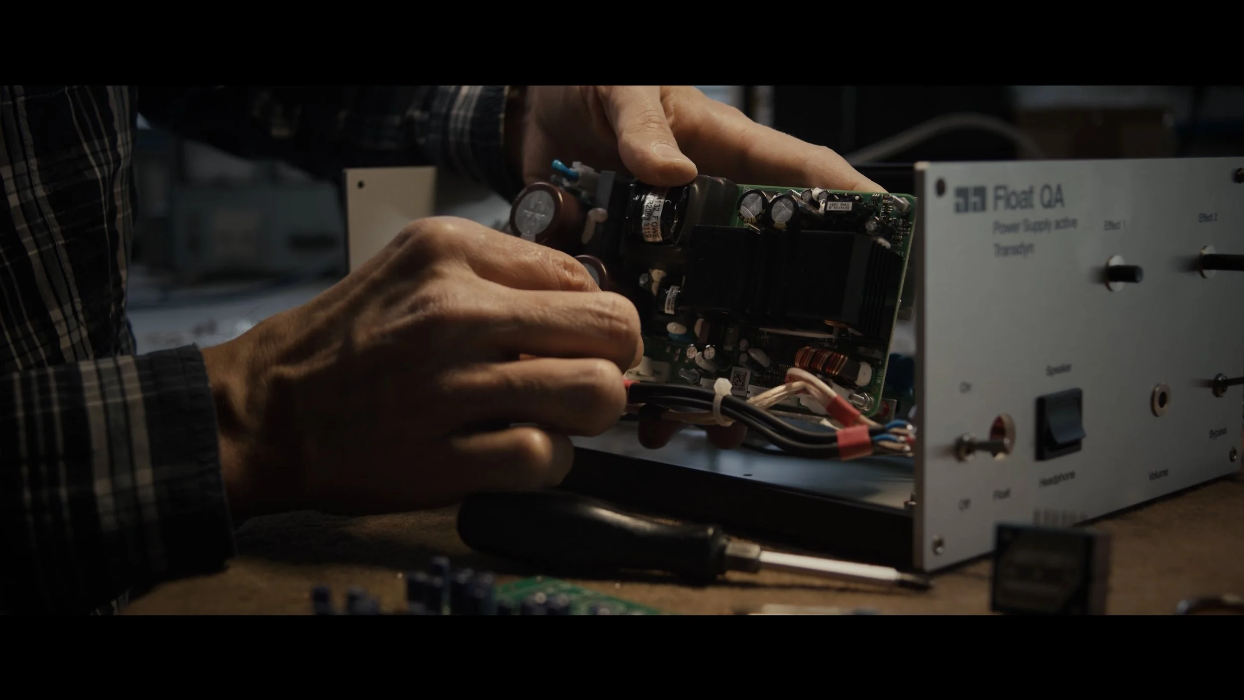 Person arbeitet an elektronischem Gerät, löten auf einer Werkbank, mit Schraubenzieher in der Hand.