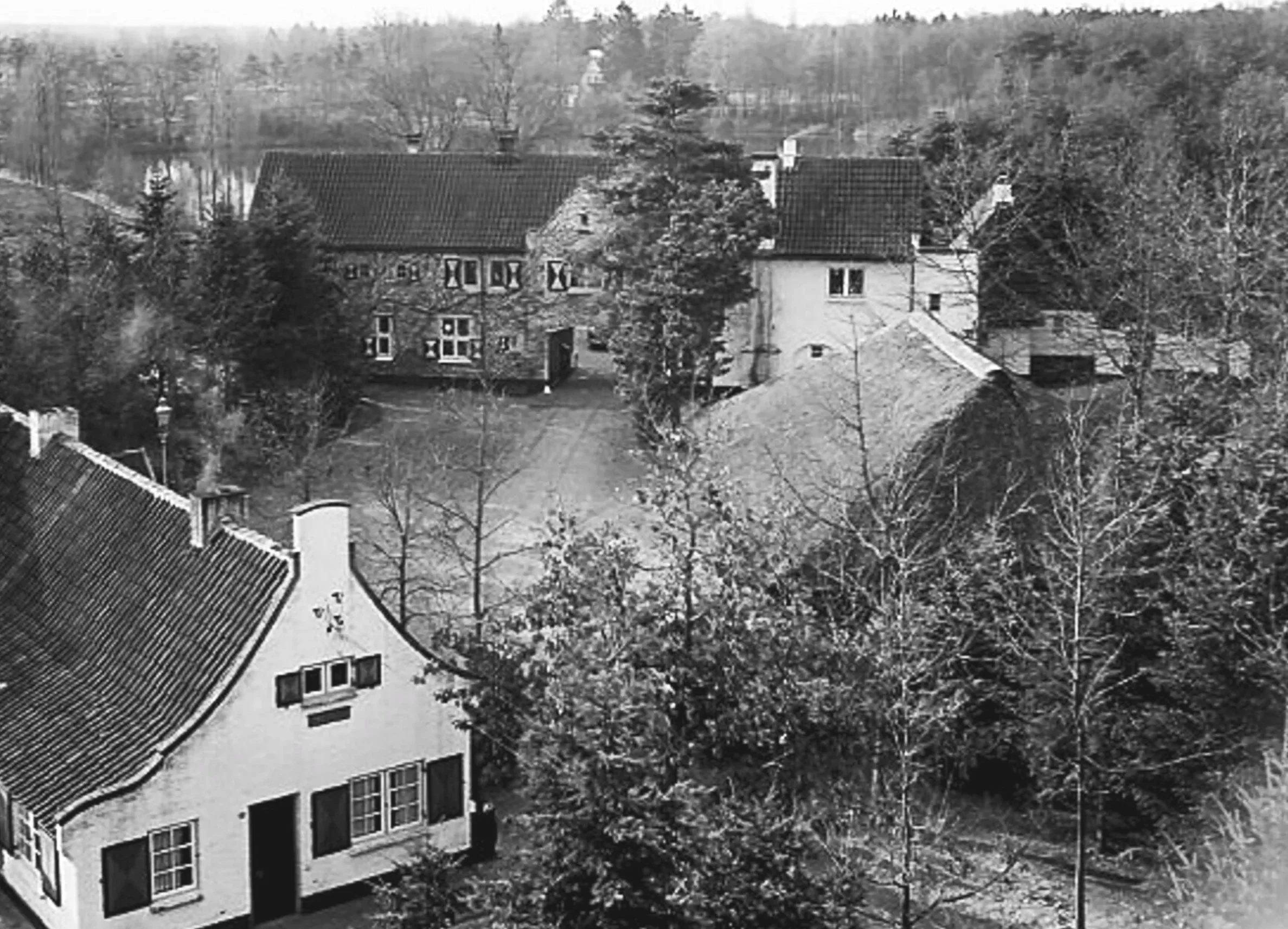 Black and white aerial photograph of residential houses surrounded by bare trees, with a hilly background of the Hulterberg in a rural or suburban setting of the estate of the Hooge Braaken.
