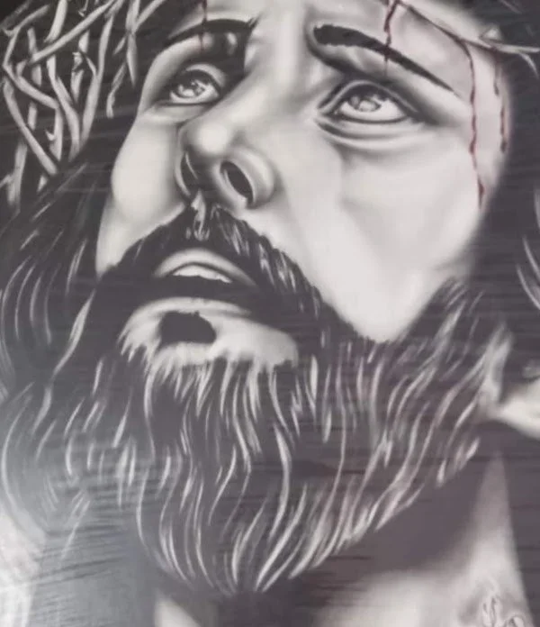 Black and white mural of Jesus Christ with a crown of thorns on his head, looking upward with a sorrowful expression, detailed beard, and flowing hair.