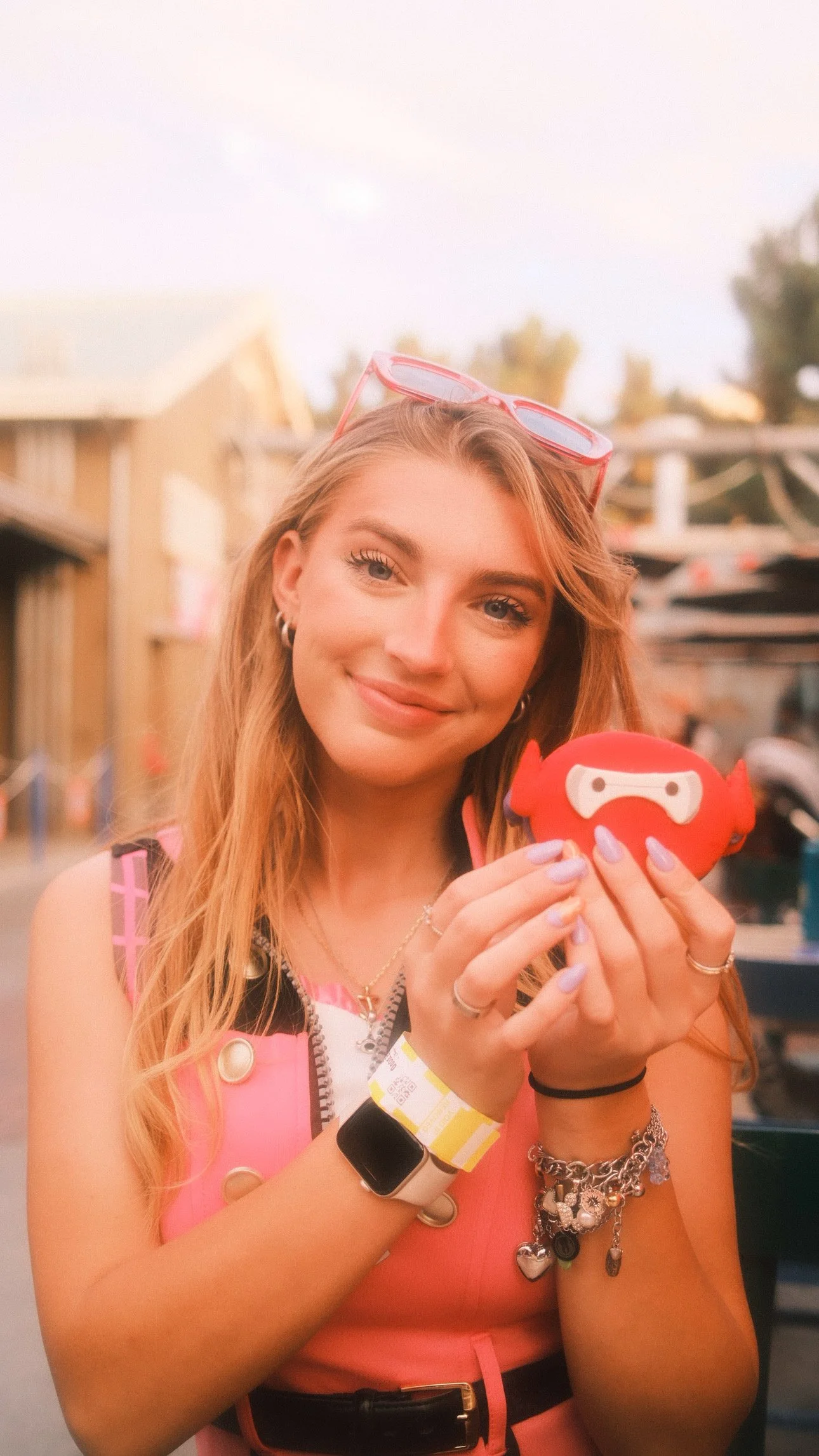 A young woman with long, wavy, light brown hair and light skin holding a red plush toy shaped like a crab at an outdoor event during sunset.
