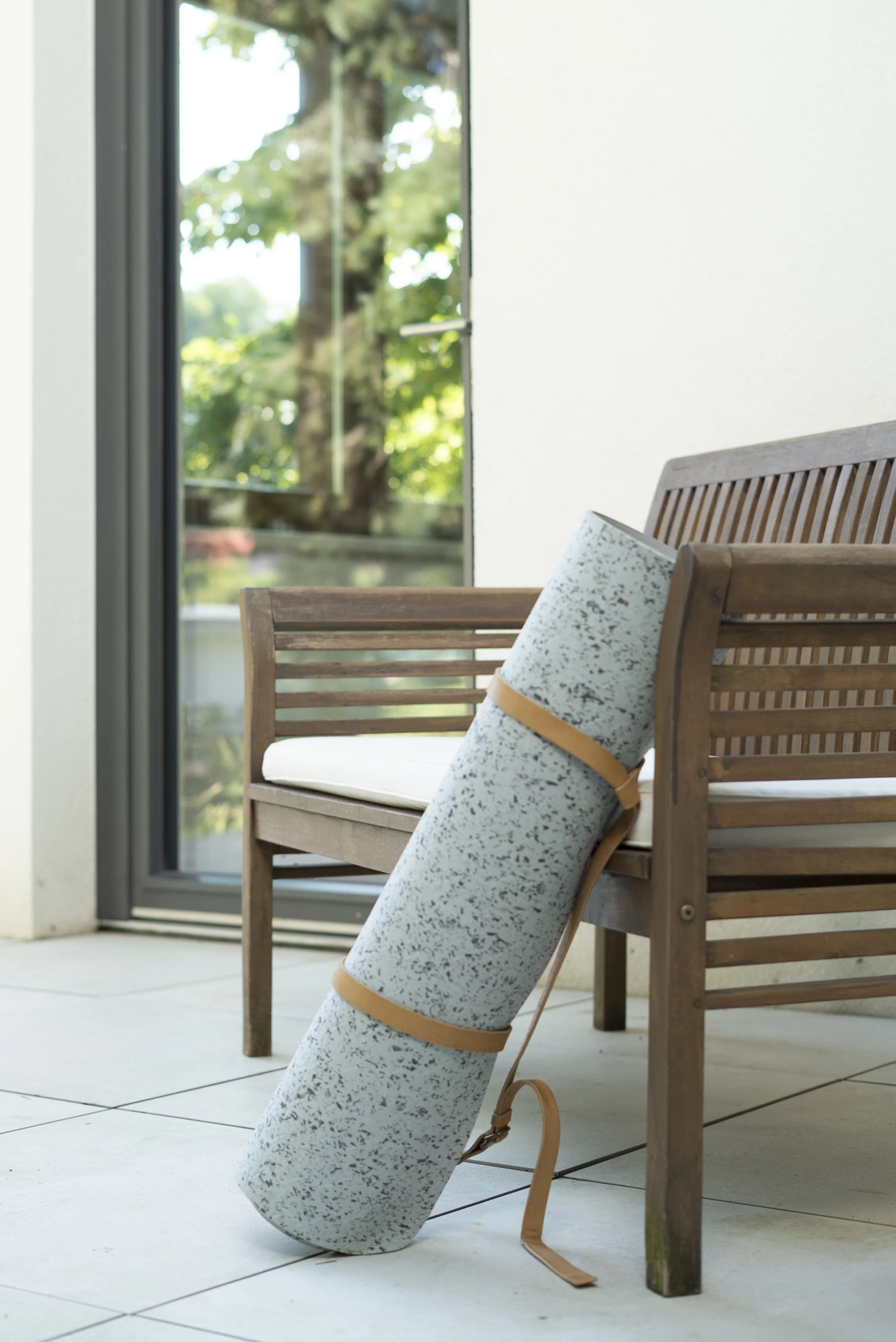 Yogastudio Krottenbachstraße 1190 Wien: Ein Yogamatte liegt an einer Holzbank auf einer Terrasse neben einer Terrassentüre aus Glas, auf der sich viel Licht und grüne Bäume spiegeln.