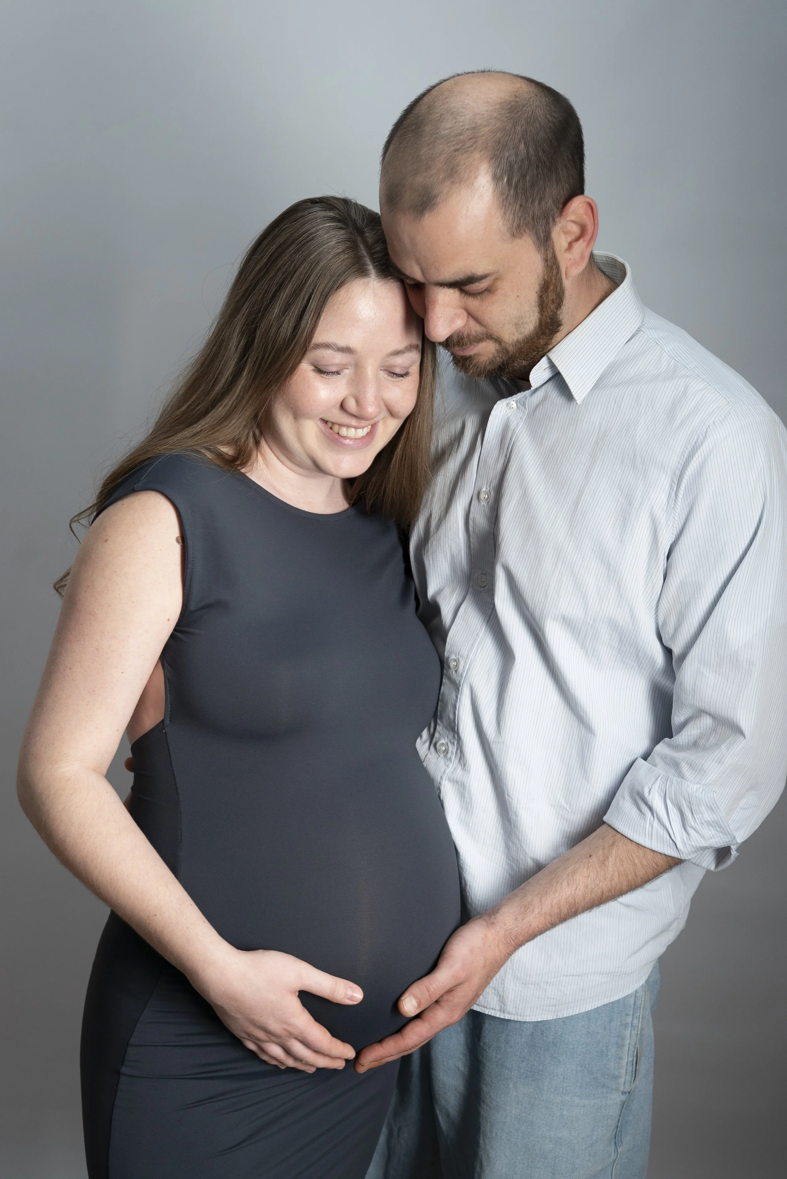 Schwangere Frau und Partner, beide halten den Babybauch und posieren für ein Foto in einem Fotostudio.