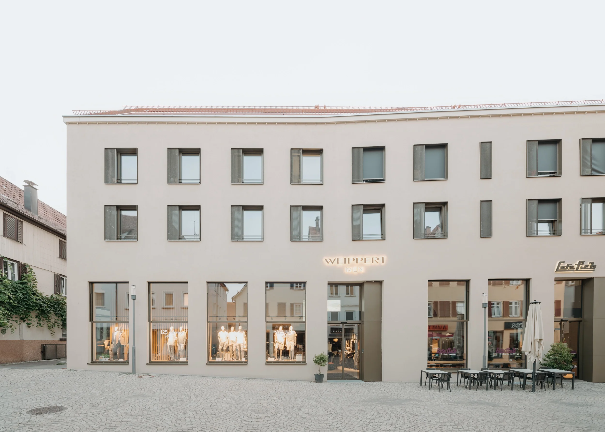 Blick auf die Ladenzeile im Erdgeschoss mit Schaufenstern von Textilhandel und Café