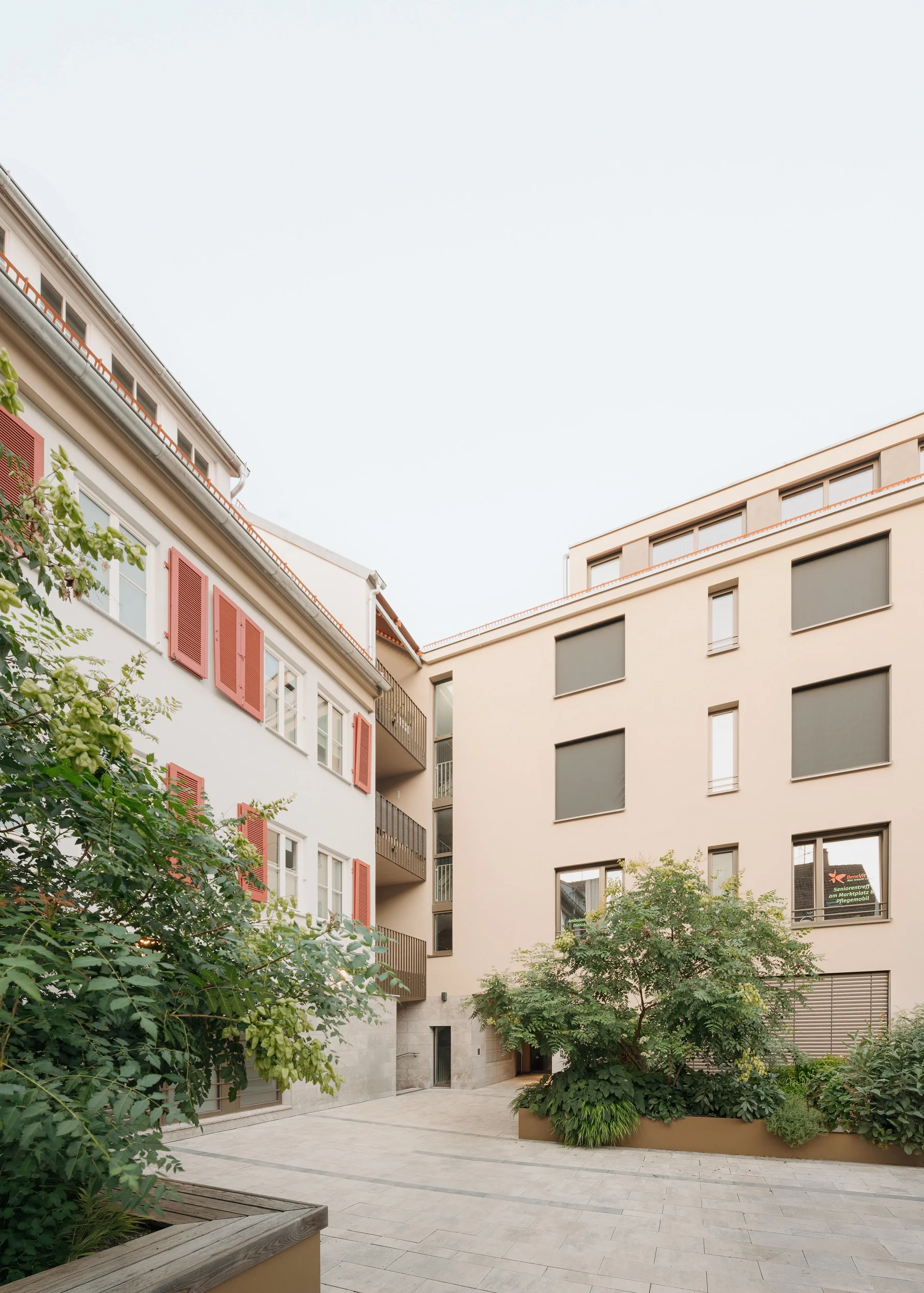 Ruhiger Innenhof mit Bepflanzung, Balkonen und textilem Sonnenschutz an der Hoffassade