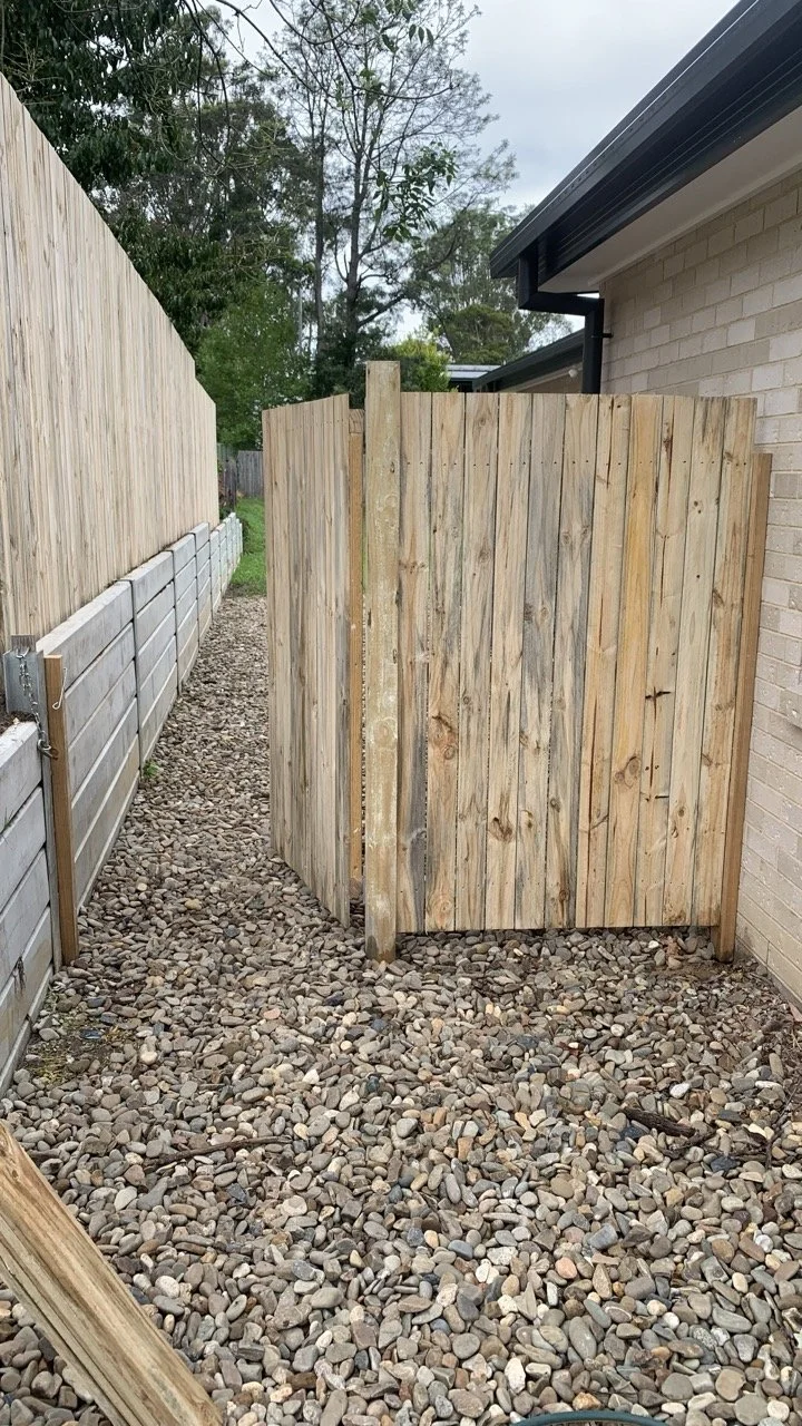 paling fence with open gate and retaining all with concrete sleepers and pebbles on the ground