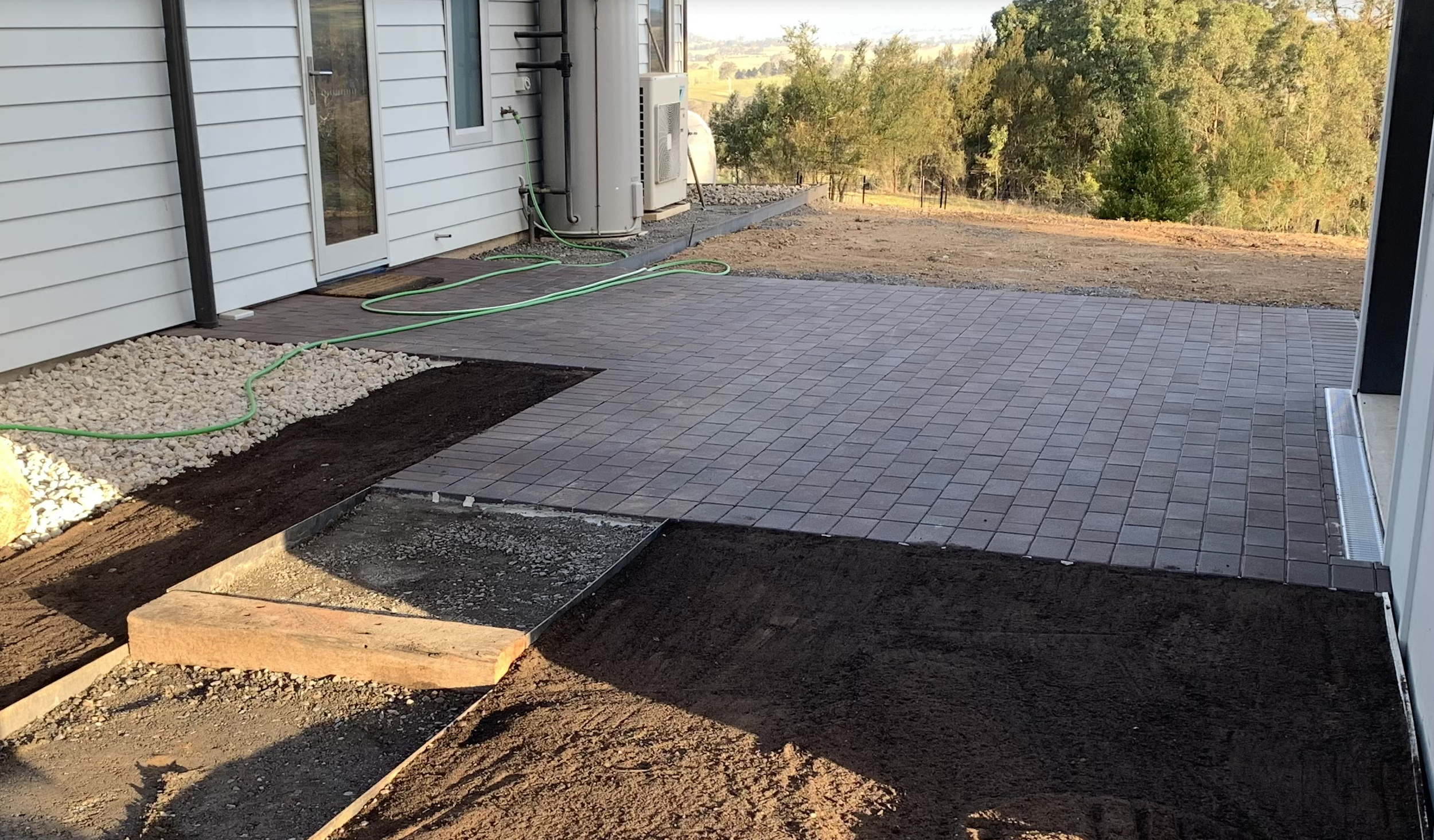 Paving area between house and carpot, surrounded with garden and lawn. there is a sleeper step with steel edging to walk to the paving area