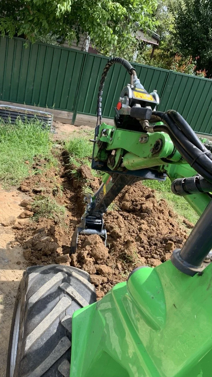 green Avant loader with digger attachment digging soil out with green trees in the background