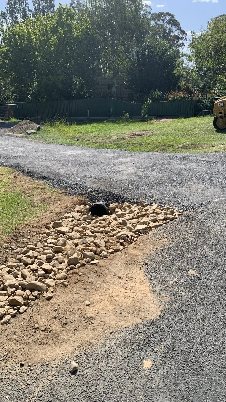road base driveway with river rocks and pipe under driveway for water drainage