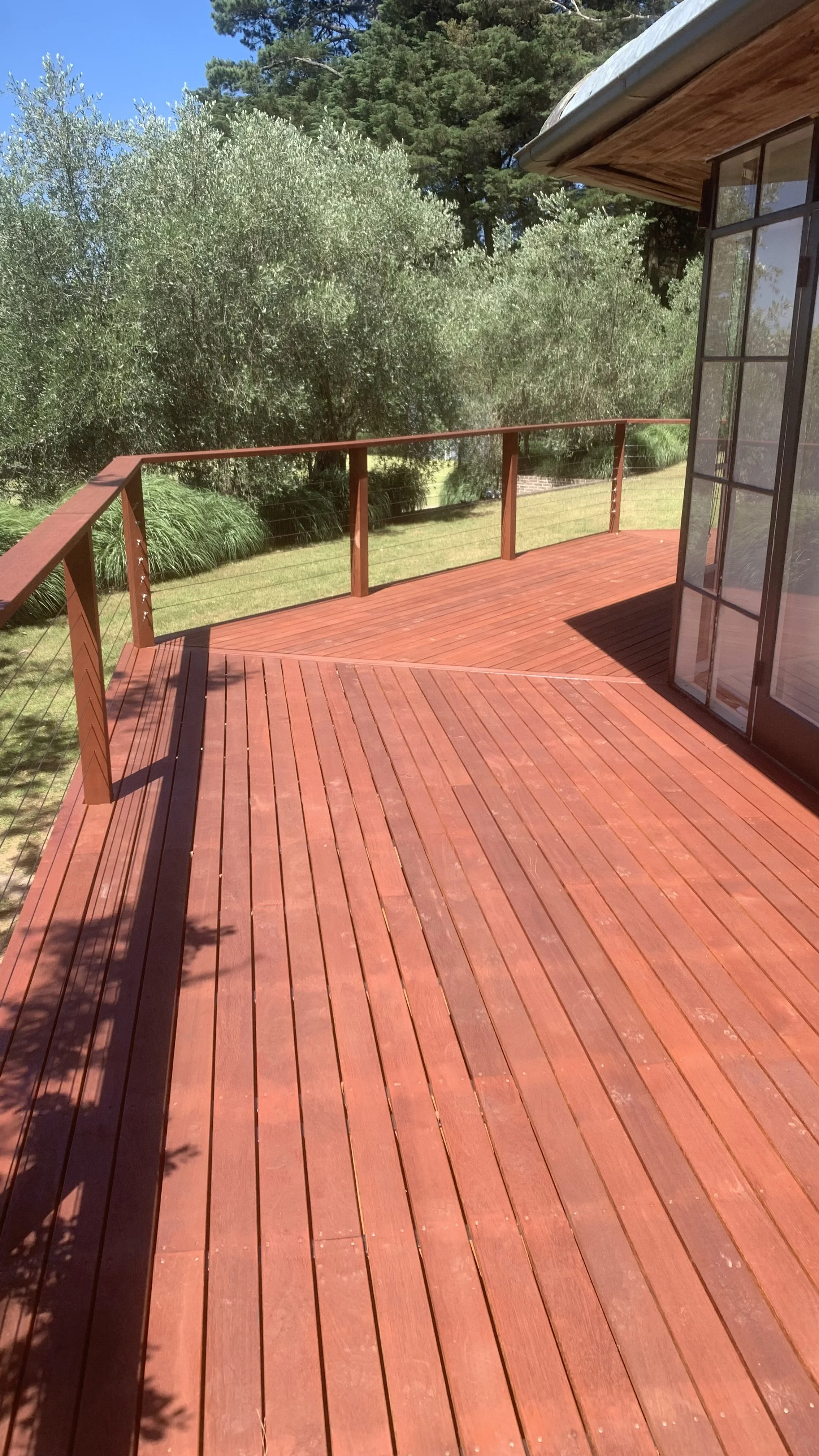 Wooden deck with wire railing, offering a clear view of the grassy lawn and trees beyond