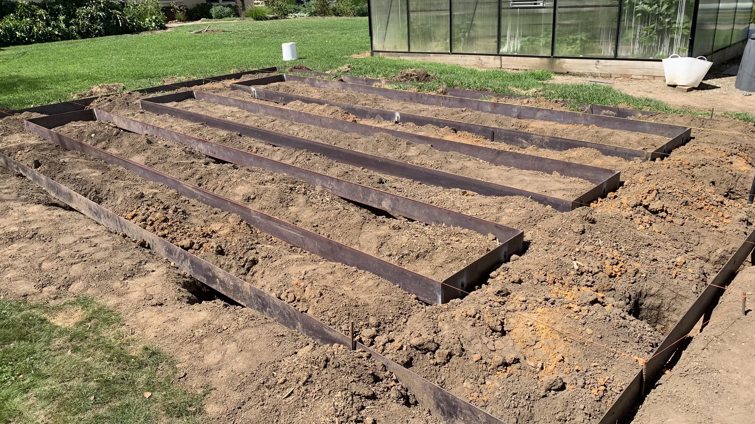 Prepared garden bed with metal edging and freshly tilled soil, ready for planting in a spacious outdoor garden area.