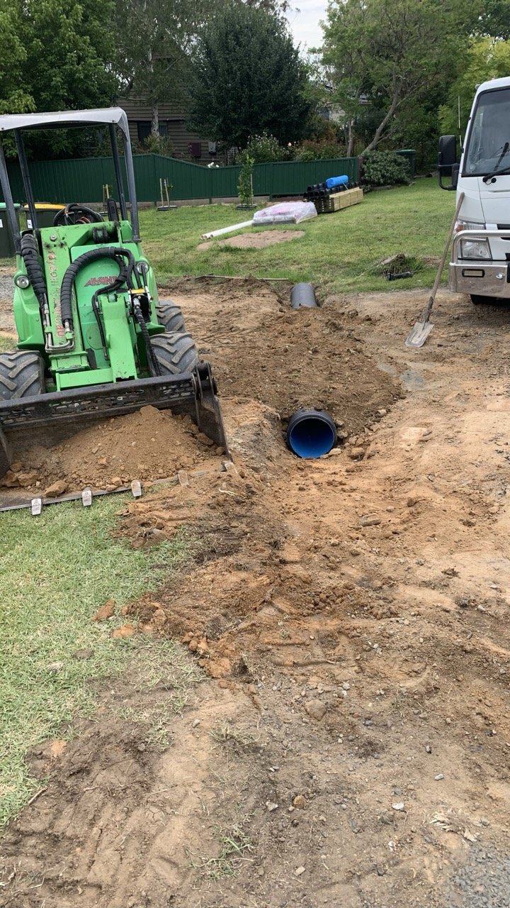 corrugated pipe installed in a trench with soil in the bucket of the Avant loader