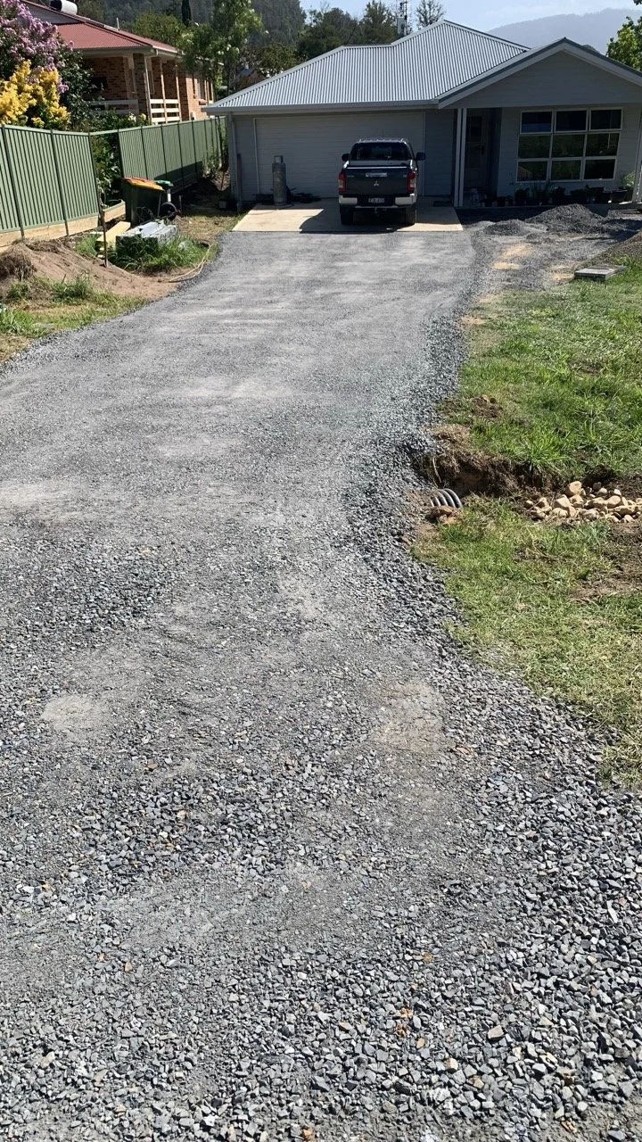 road base driveway with river rocks and pipe under driveway for water drainage