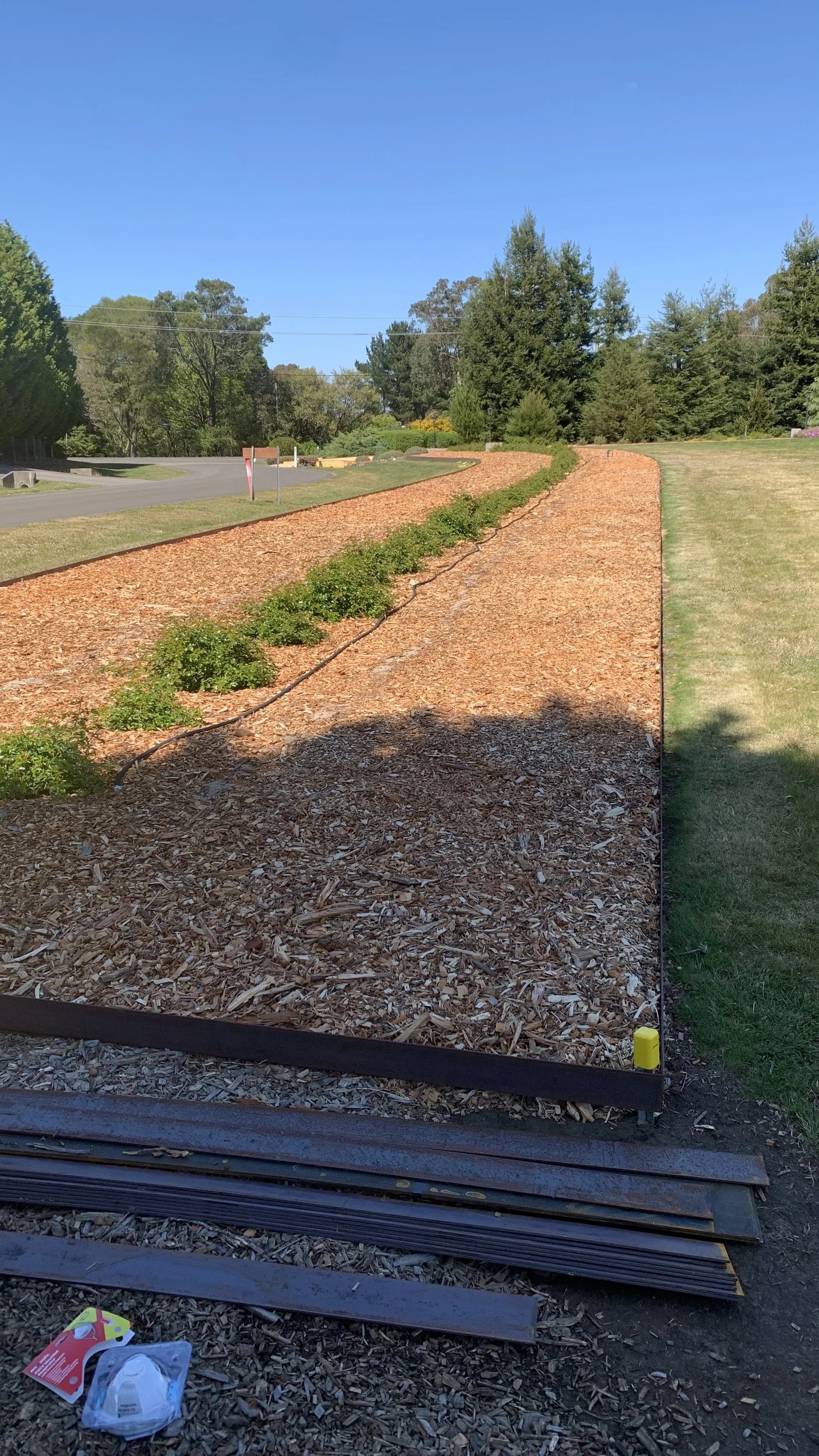 Long garden bed with steel edging and mulch, showcasing a neat and tidy outdoor landscaping project with plant rows