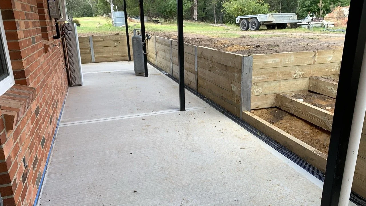 Retaining wall with steps around concrete slab. Drainage and backfill soil behind the retaining wall. a brick house on the left