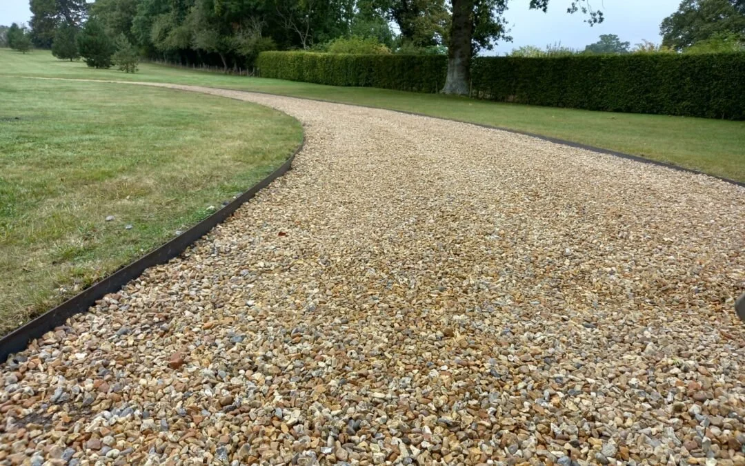 A curved gravel pathway bordered by a black edging, with green grass and trees in a park-like setting.