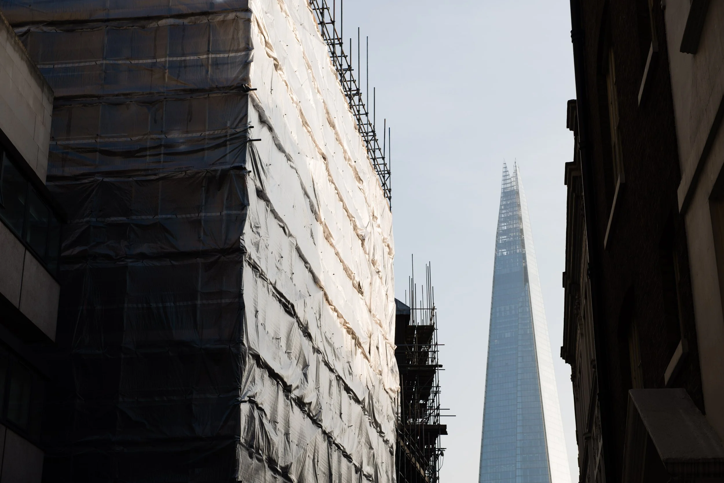 City street scene with a modern skyscraper in the distance, partially covered building under construction on the left, and an older building on the right.