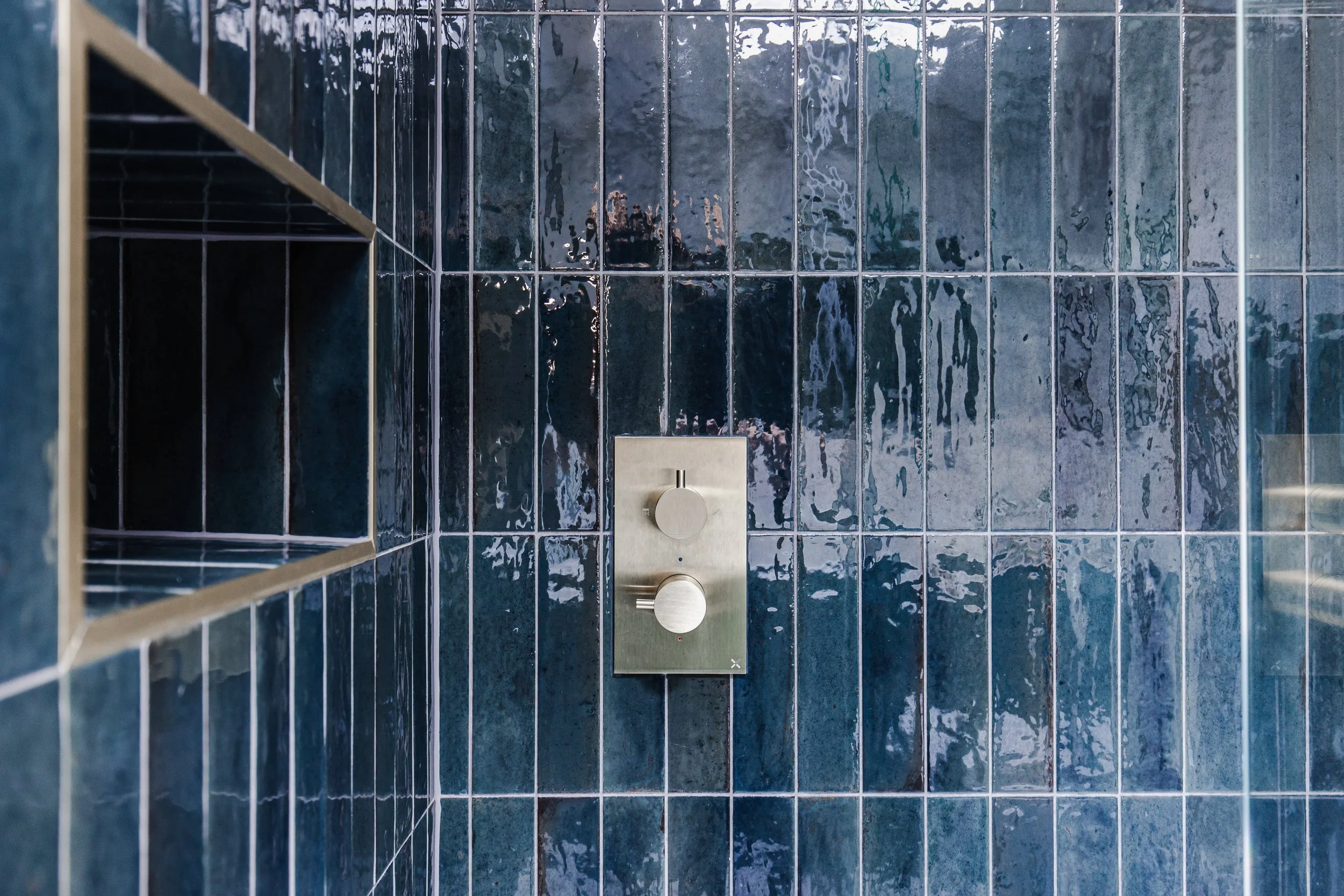 A shower with blue ceramic tiles and a metallic shower control panel.