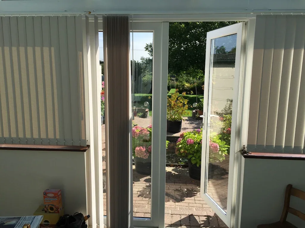 Open door leading to a backyard garden with potted pink and green flowering plants and lush green trees.
