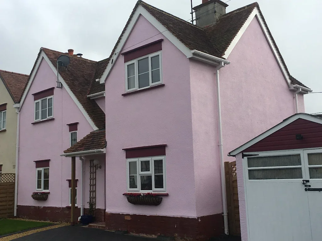 Three-story pink house with white trim and brown roof, with window flower boxes and a garage.