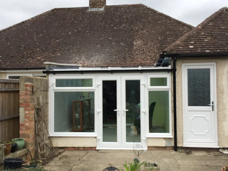 Backyard view of a house with a conservatory extension featuring white frame doors and windows, adjacent to a traditional brick and stucco wall, with a tiled roof and a small side door.