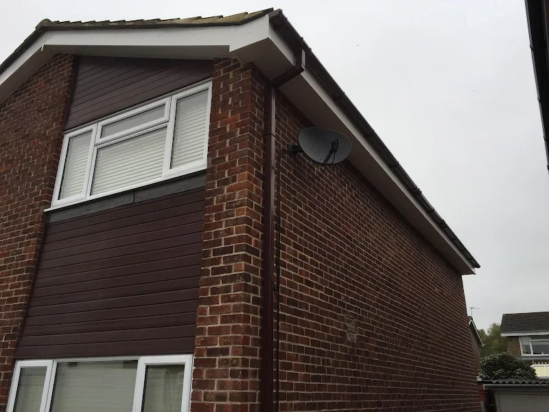 Corner of a brick house with white-framed windows, brown siding, a satellite dish attached to the wall, and a gray, overcast sky.