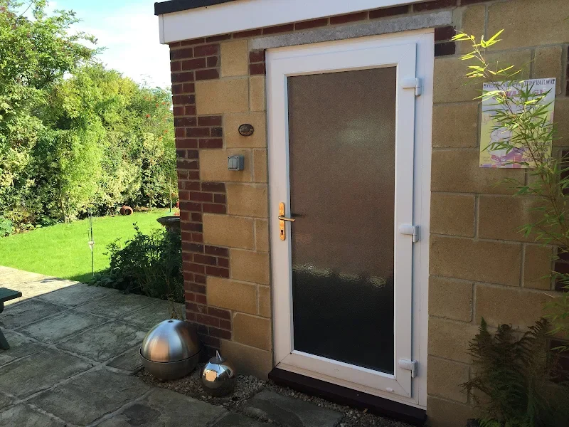 Exterior of a building with a door and a garden in the background, including a metal ball and watering can on the ground.