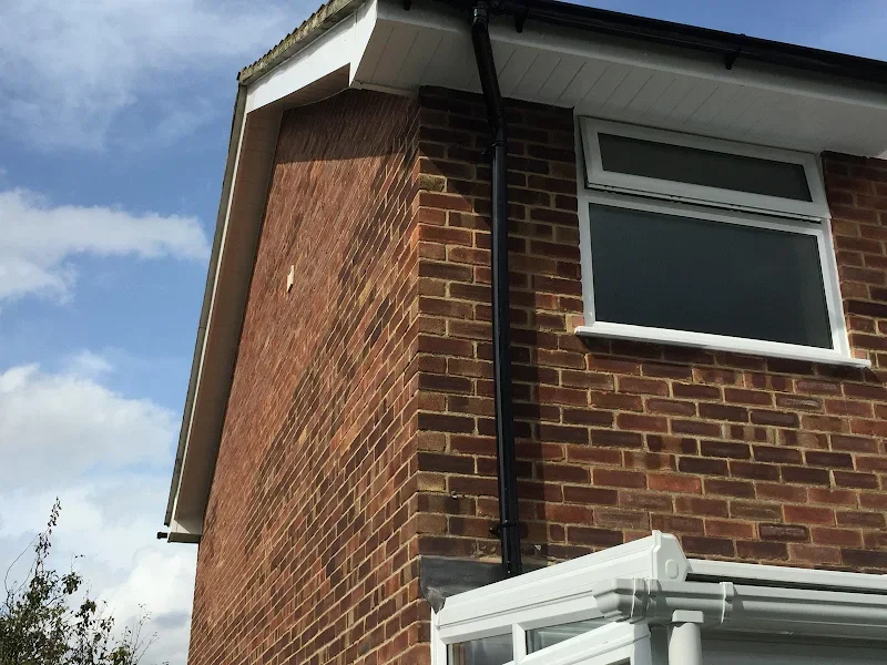 Close-up of a brick house corner showing a window, black rain gutter, and white conservatory extension.