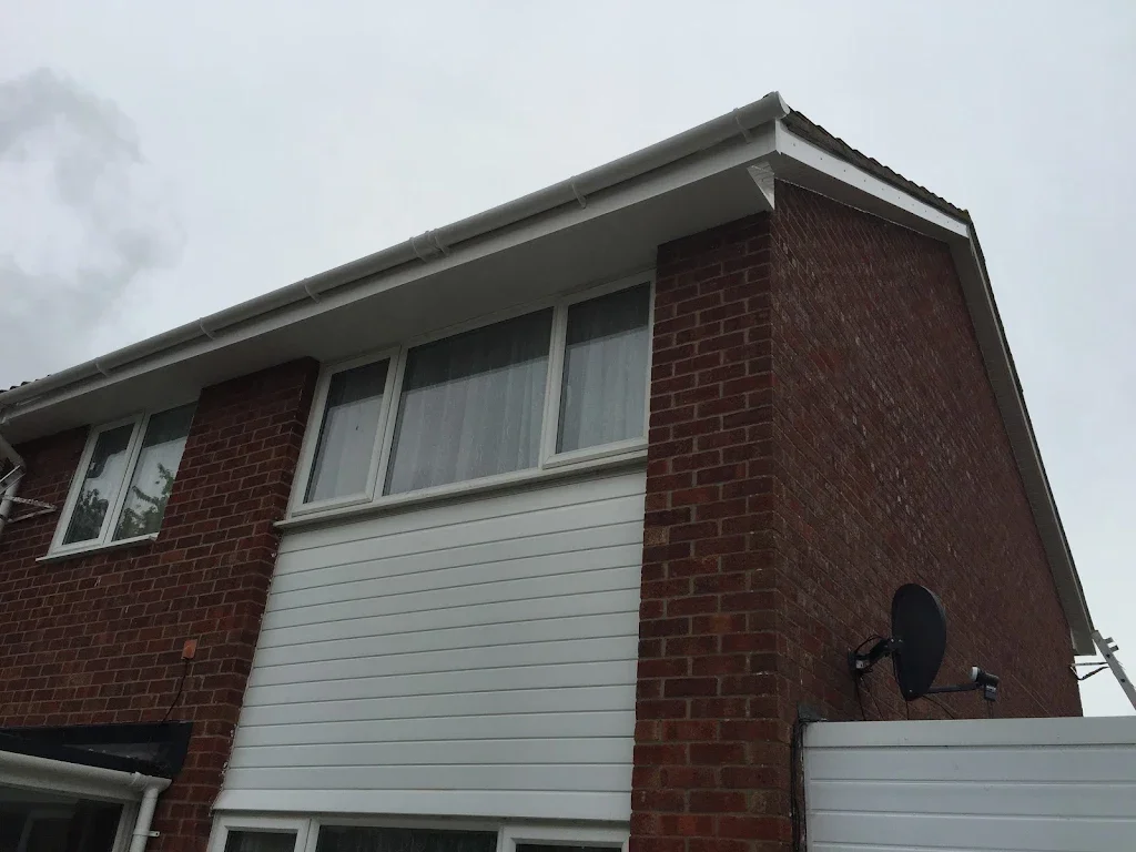A two-story brick house with white siding on the upper level, windows, and a satellite dish attached to the side.