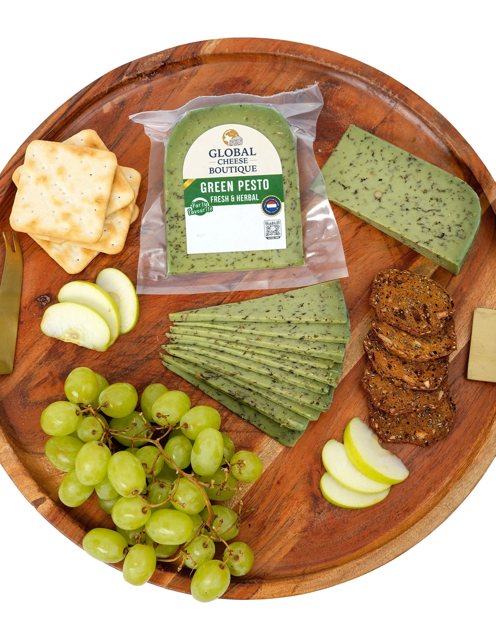 Green Pesto Gouda 180 g, sealed pack, wedge and slices on a round wooden tray with grapes and apple