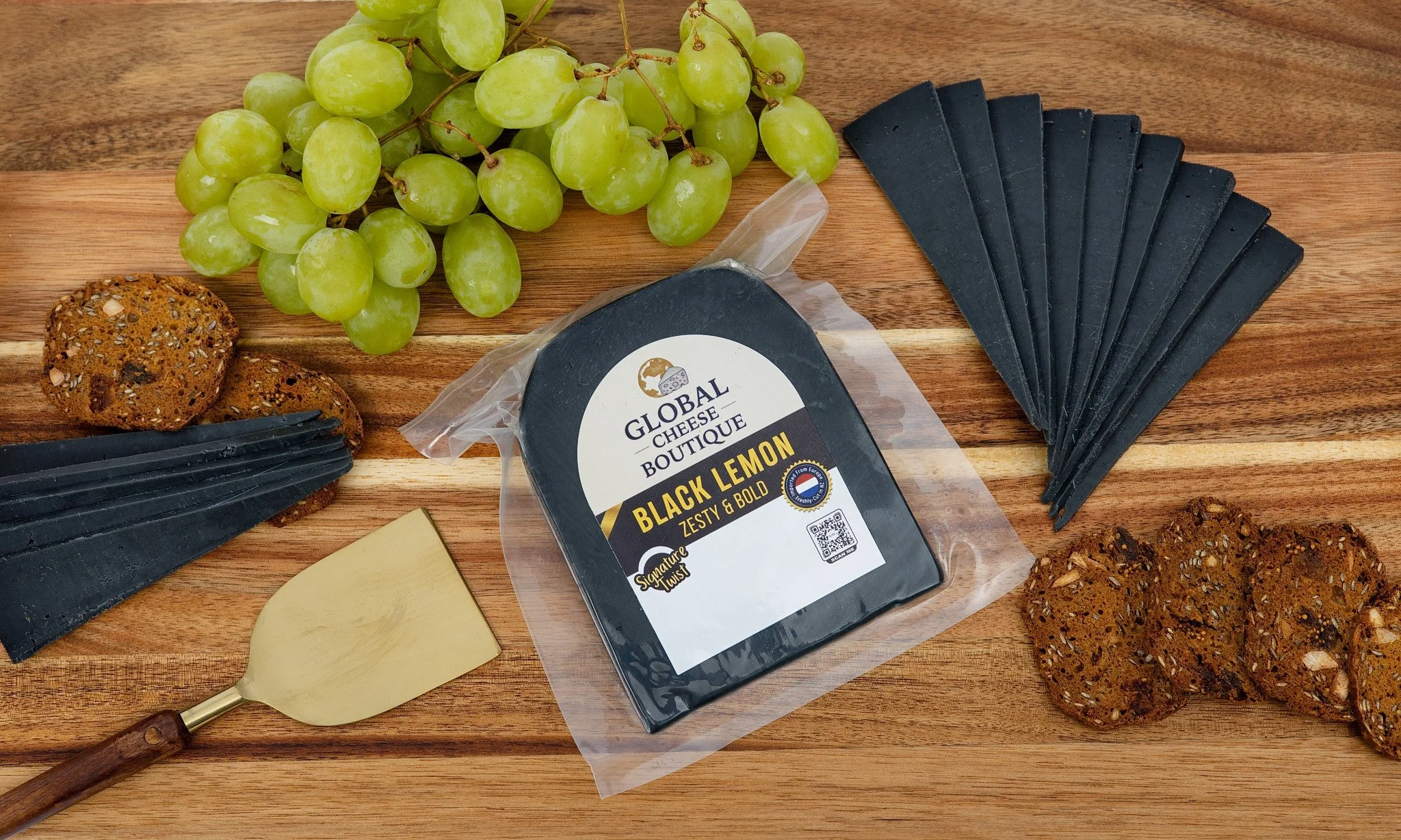 Black Lemon Gouda 180 g, sealed pack and fanned slices on a board with grapes