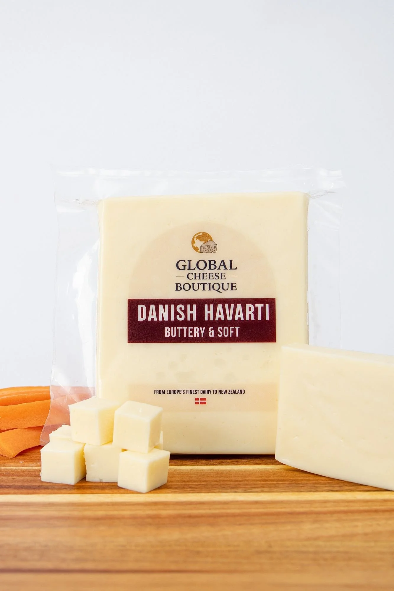 Danish Havarti, sealed pack with a cut cheese piece and cubes on a wooden board